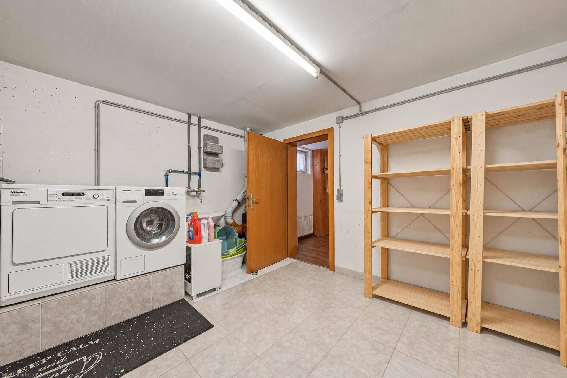 Hauswirtschaftsraum im Untergeschoss mit Waschmaschine, Trockner und Holzregalen für Vorräte.