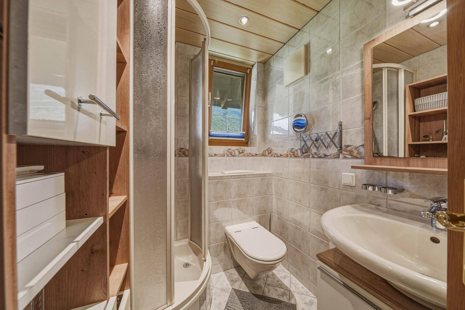 Kleines Badezimmer mit Duschkabine, WC, Waschbecken und Fliesenboden in hellen Grautönen.