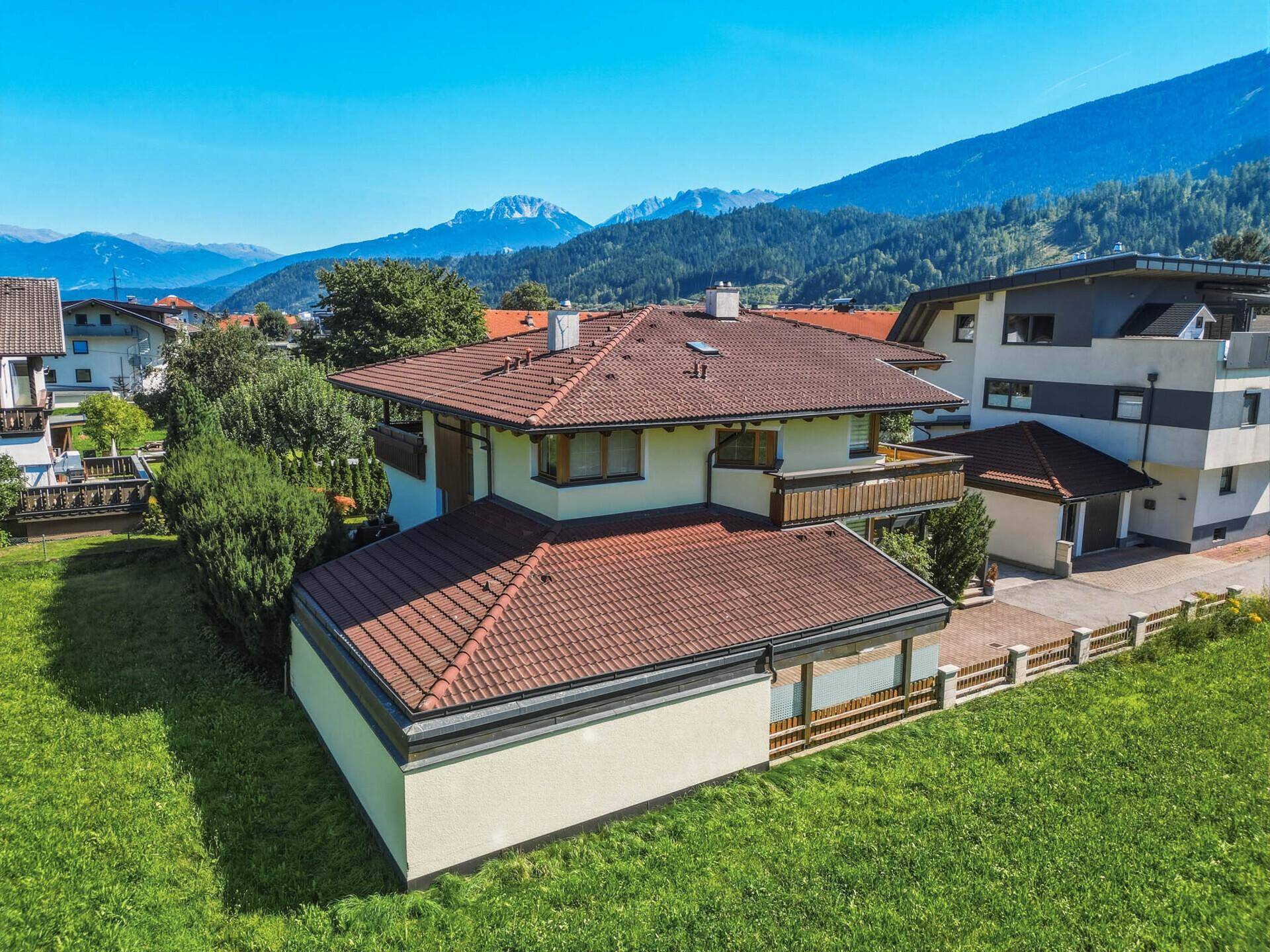 Luftaufnahme des Hauses von der Seite, mit rotem Ziegeldach und Blick auf die Berge.