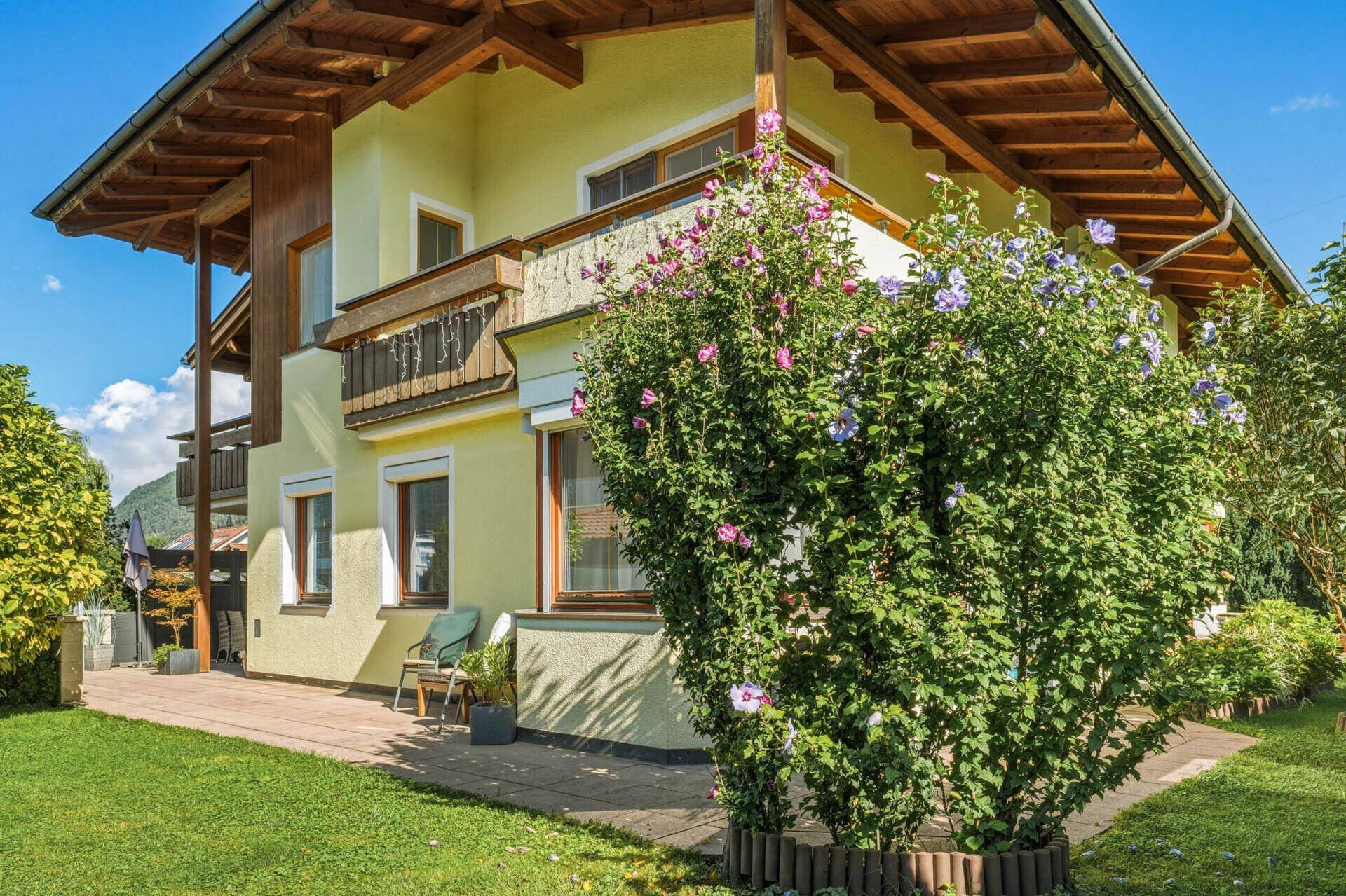 Gepflegter Gartenbereich mit Rasenfläche und einem großen blühenden Strauch neben dem Haus.