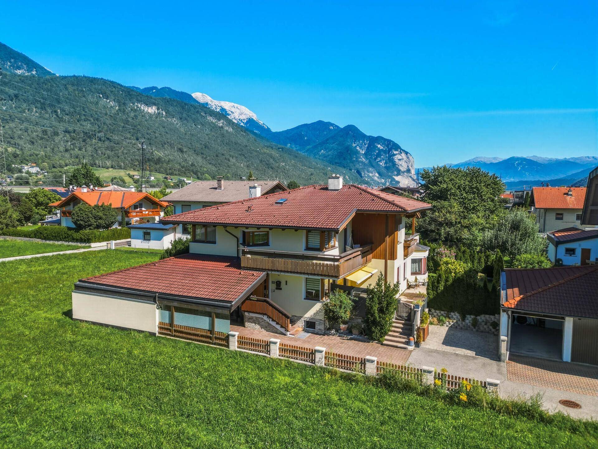 Luftaufnahme des Hauses mit rotem Ziegeldach, umgeben von Grünflächen und Bergen.