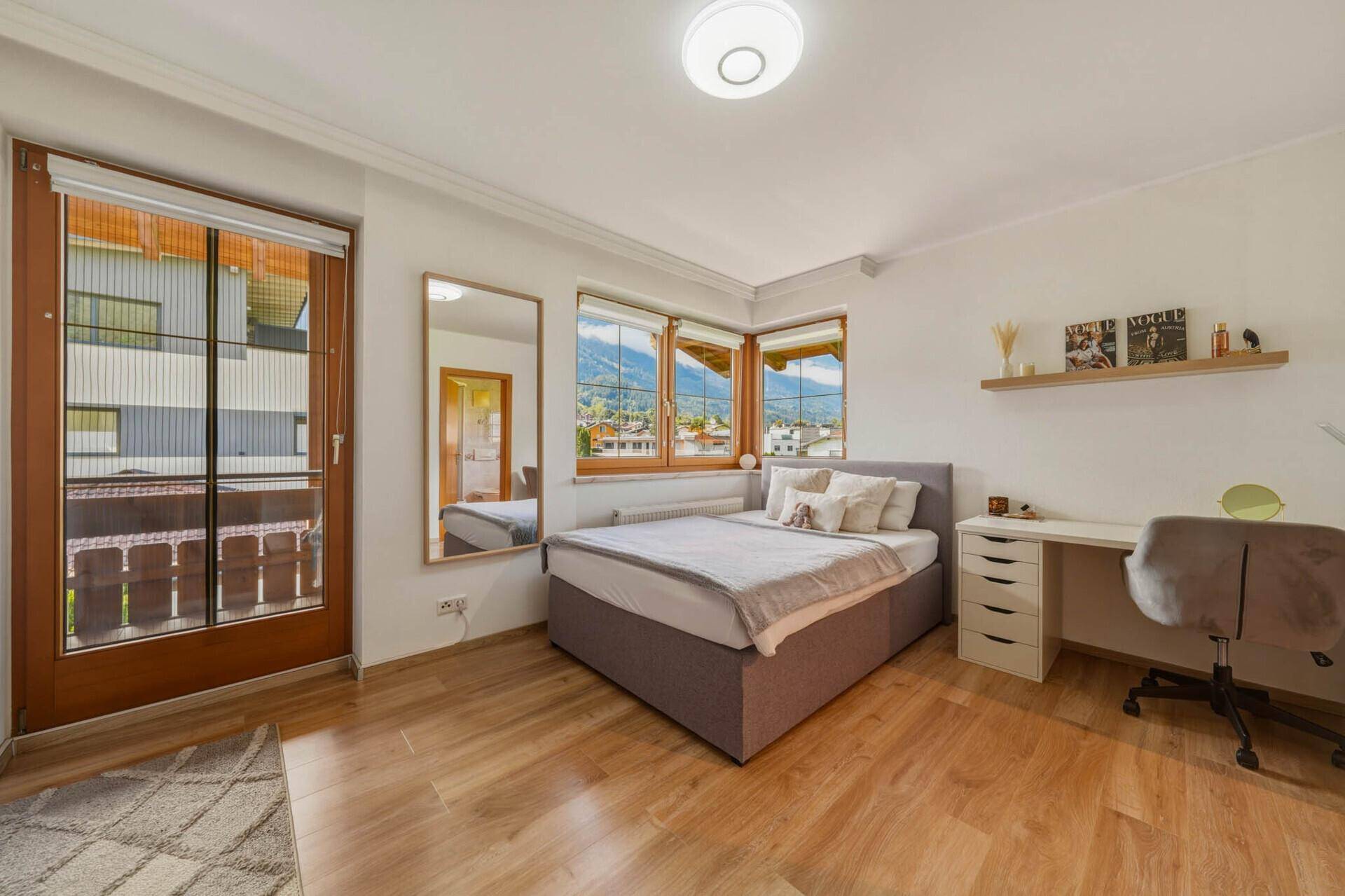 Helles Schlafzimmer mit Einzelbett, Schreibtisch und Balkonzugang.