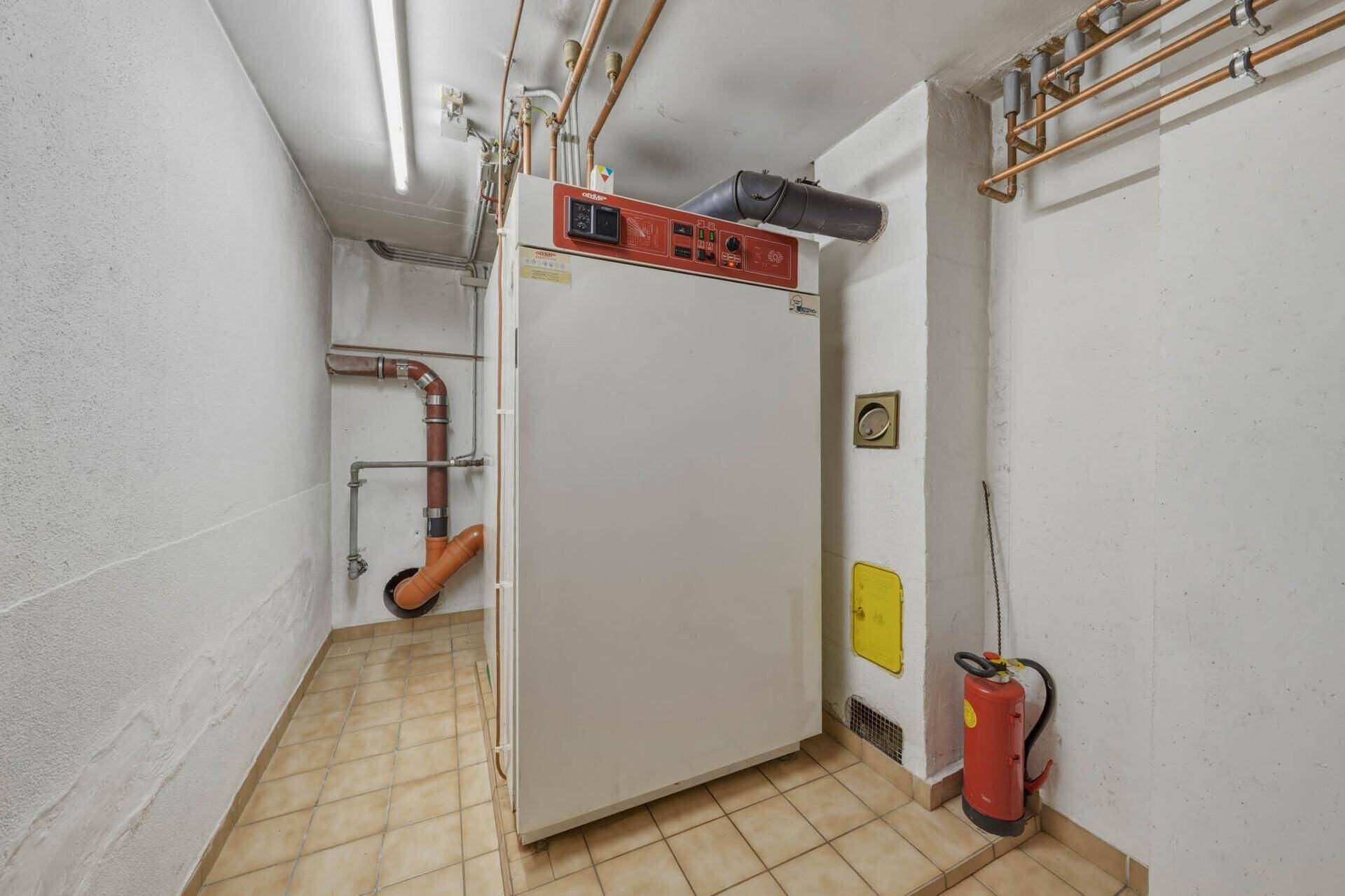 Heizungsraum im Untergeschoss mit großem Heizkessel und sichtbaren Rohren.