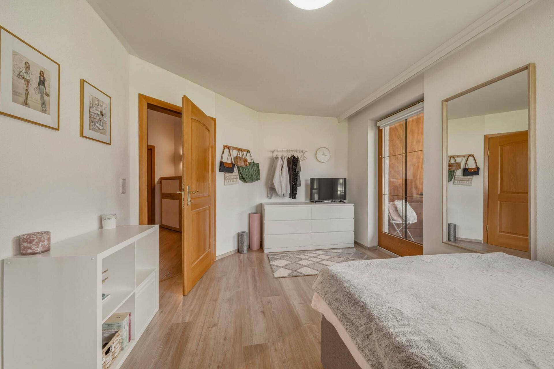 Schlafzimmer mit Bett, Kommode und großem Spiegel, hell und geräumig.