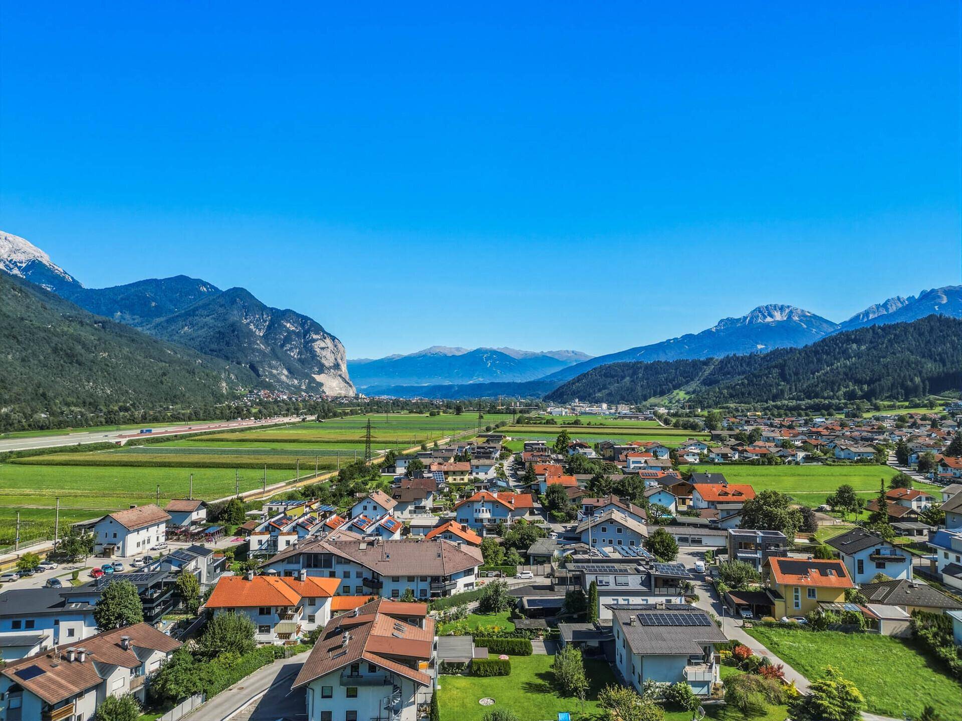 Weitläufige Luftaufnahme einer Siedlung in einem Tal, umgeben von majestätischen Bergen.