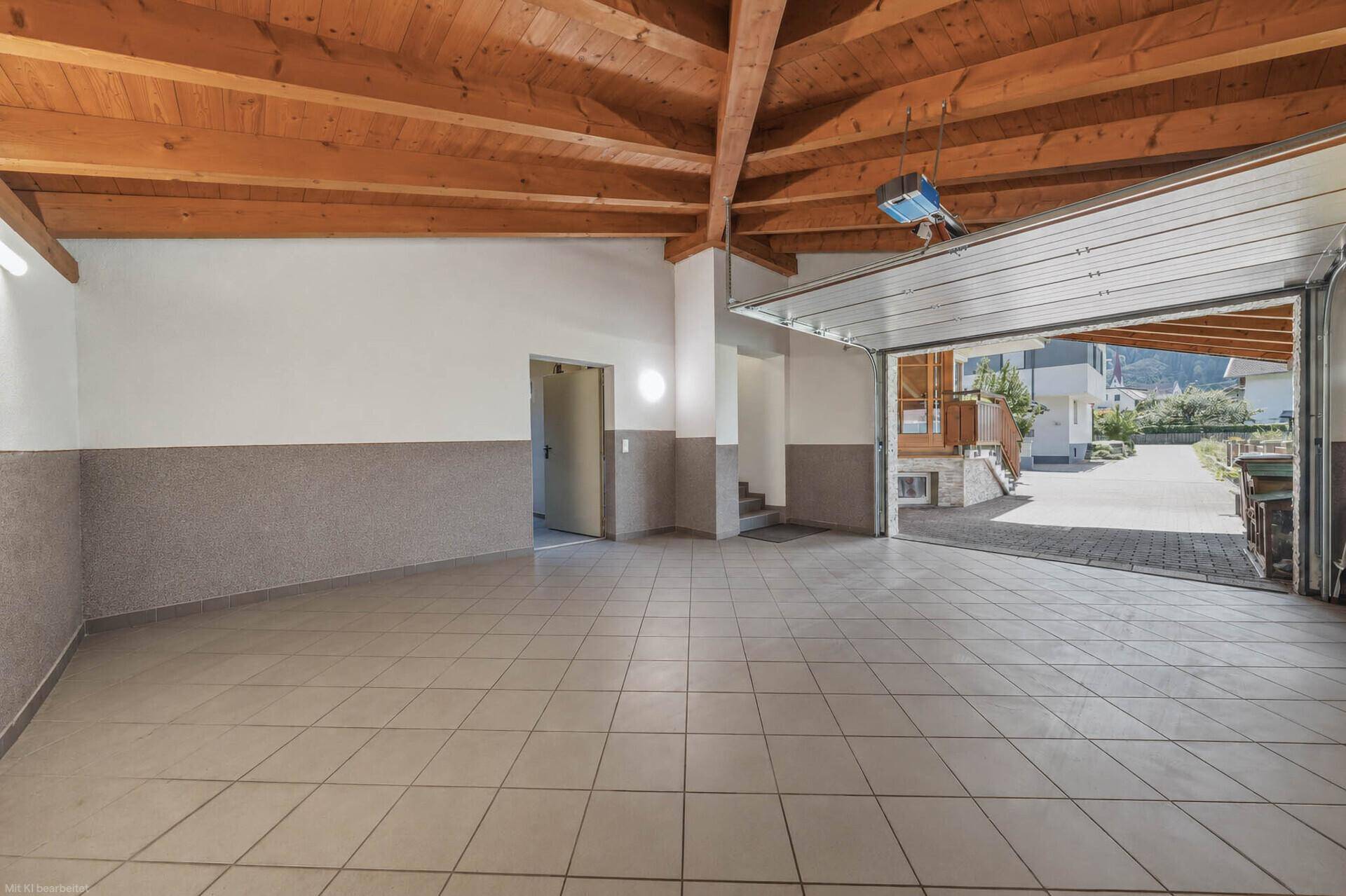 Helle Garage mit offenem Tor, Fliesenboden und Blick auf die gepflasterte Einfahrt.