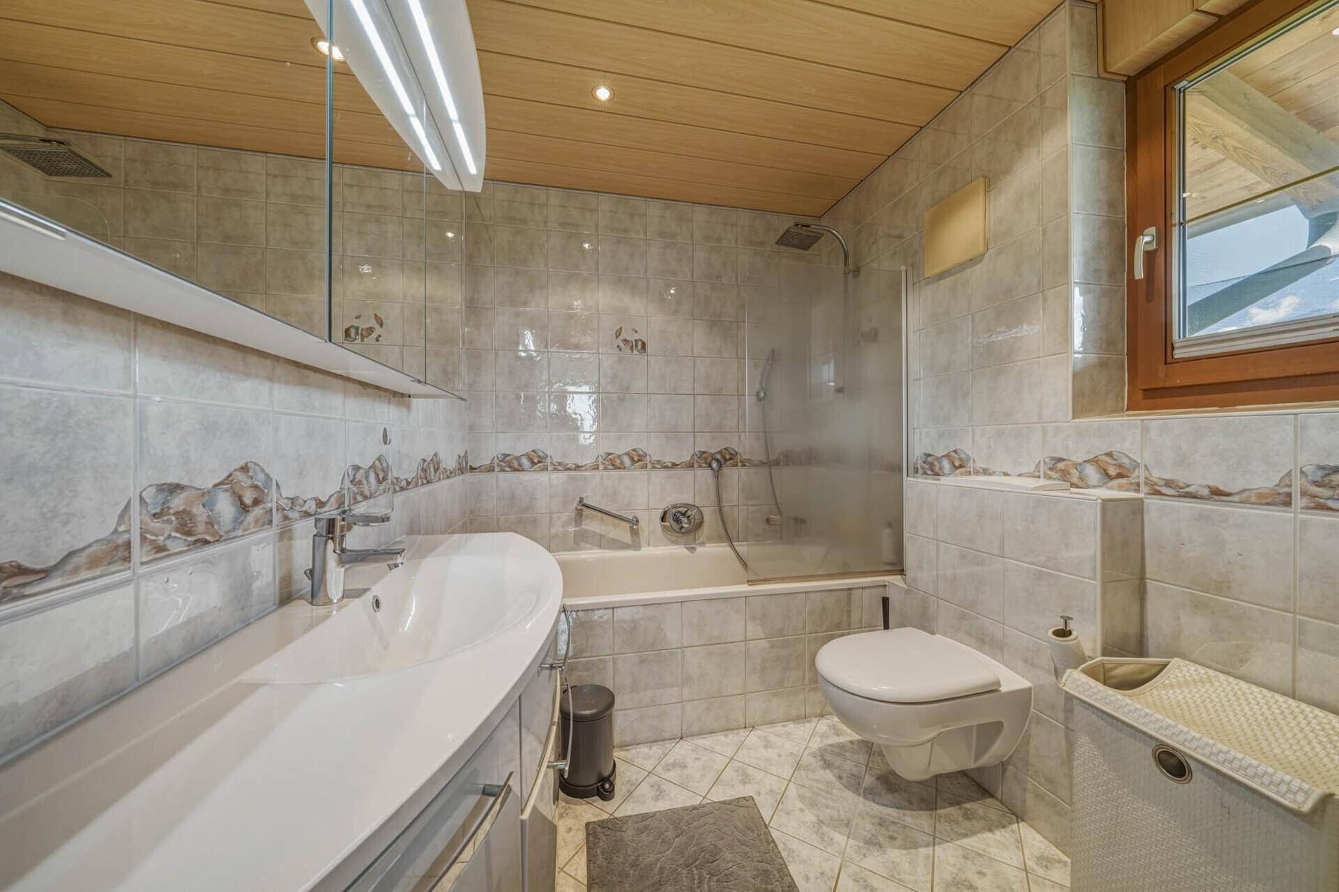 Badezimmer mit Badewanne, Duschfunktion, WC und Holzdecke.