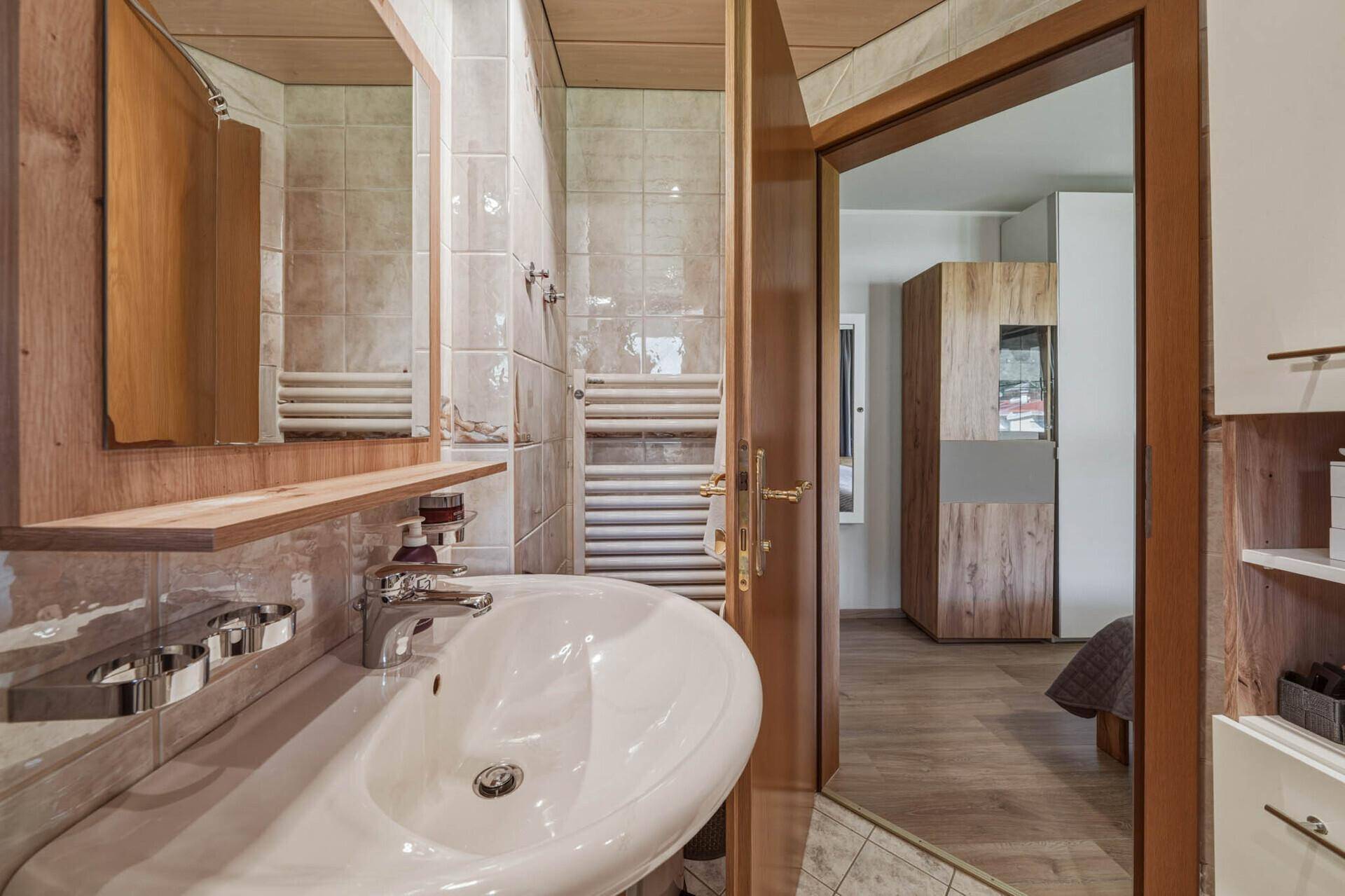 Badezimmer mit Waschbecken, Spiegel und Zugang zu einem weiteren Raum, möglicherweise einem Schlafzimmer.