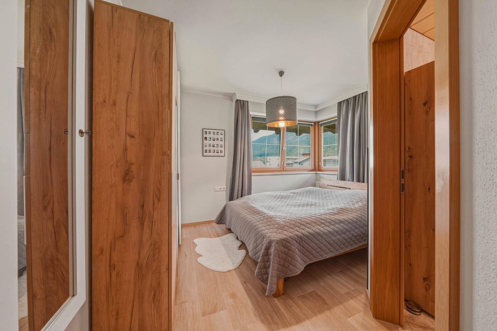 Gemütliches Schlafzimmer mit Holzboden, Doppelbett und Blick auf die Berge durch das Fenster.