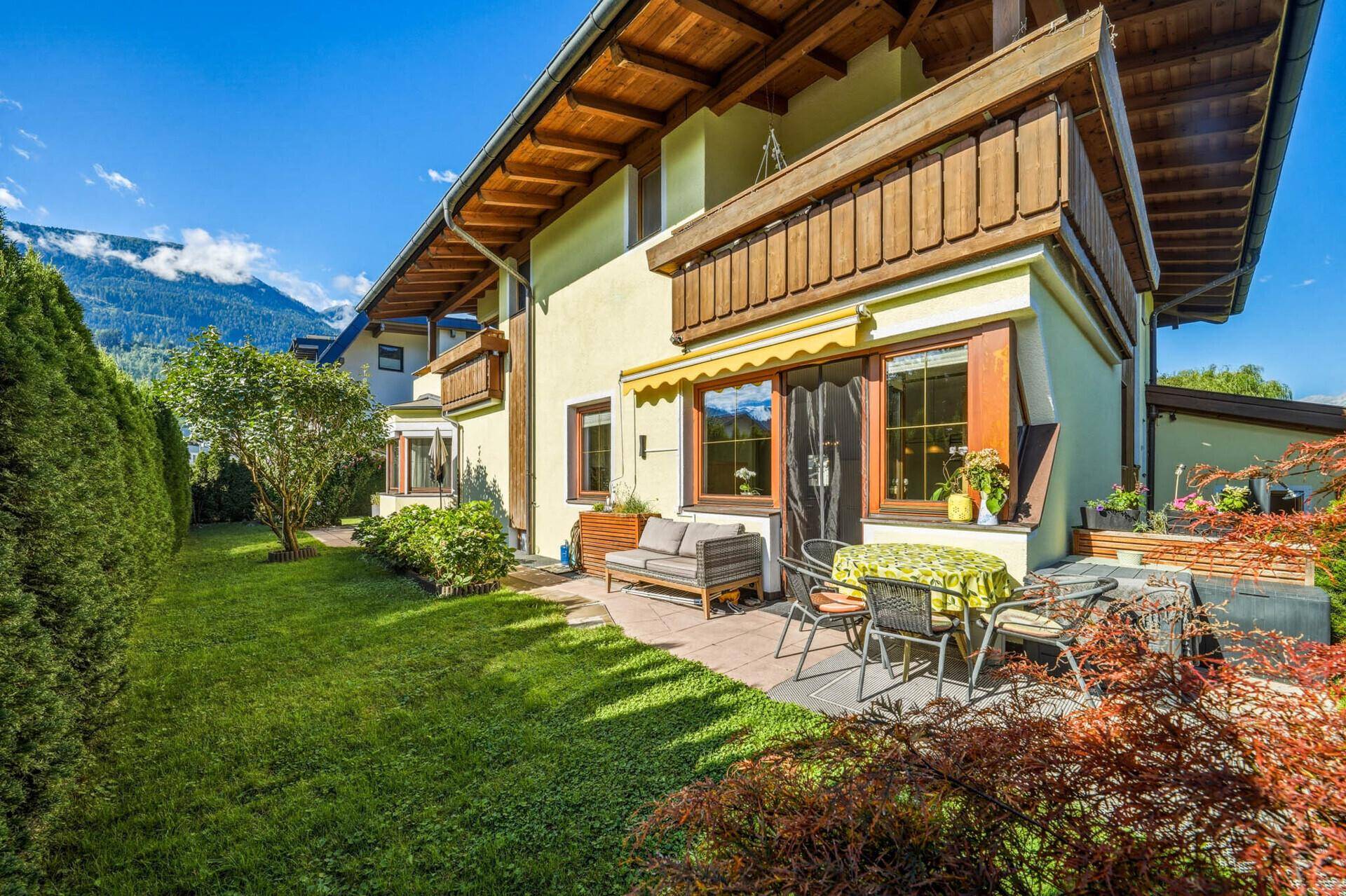 Weitläufige Terrasse mit Gartenmöbeln und Rasenfläche, umgeben von üppigem Grün und Bergblick.