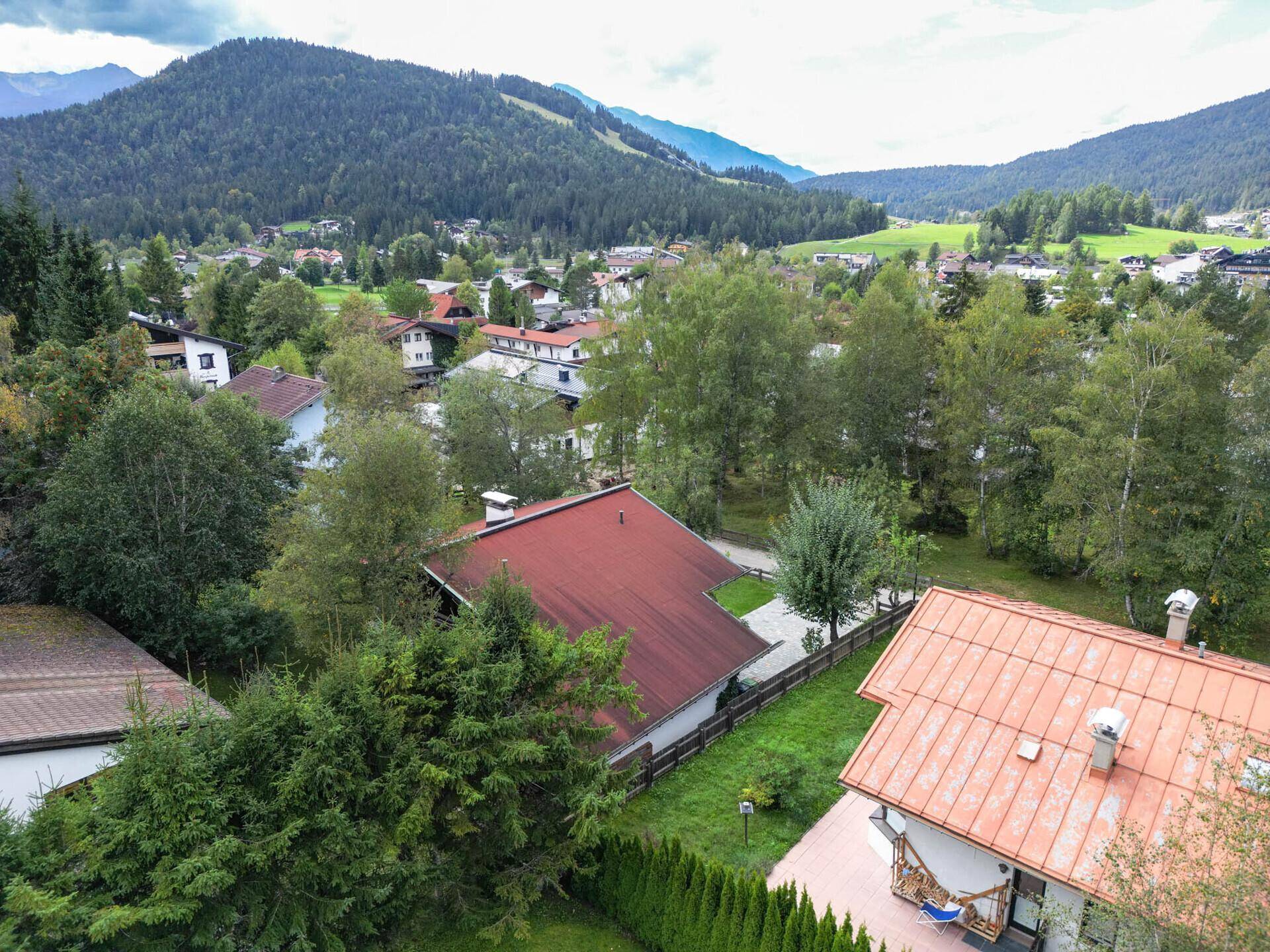 Luftaufnahme von Wohnhäusern mit roten Dächern, umgeben von grünen Hügeln und Bergen.