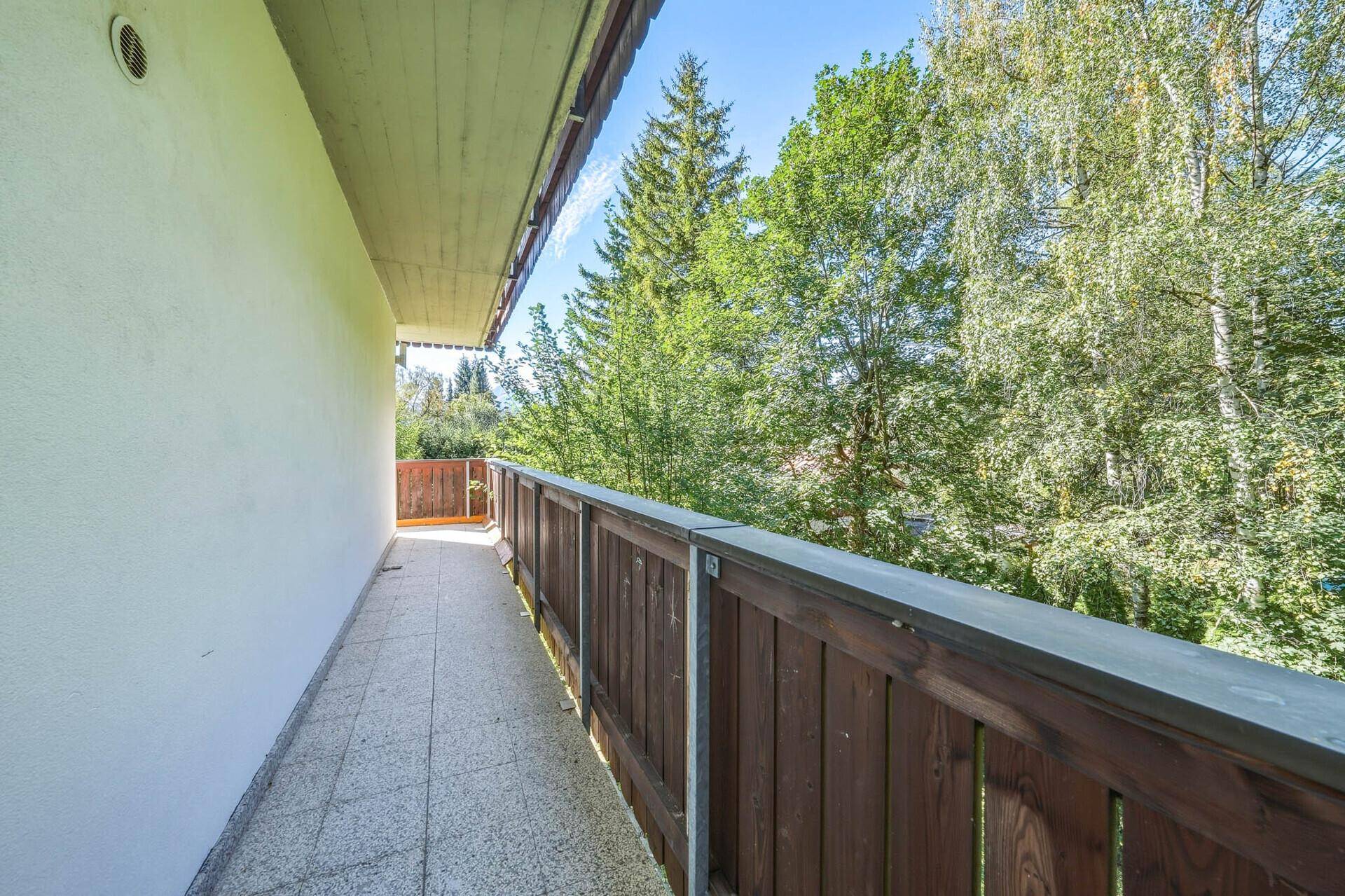 Schmaler Balkon mit Holzelementen und Blick auf hohe Bäume.