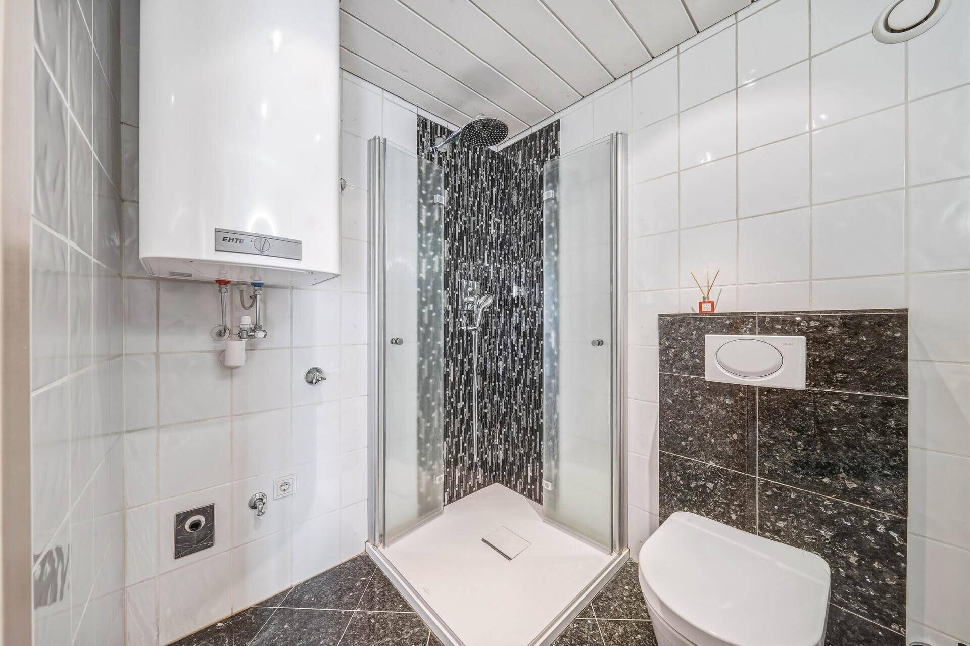 Funktionales Badezimmer mit Duschkabine, Wandtoilette und Warmwasserboiler.