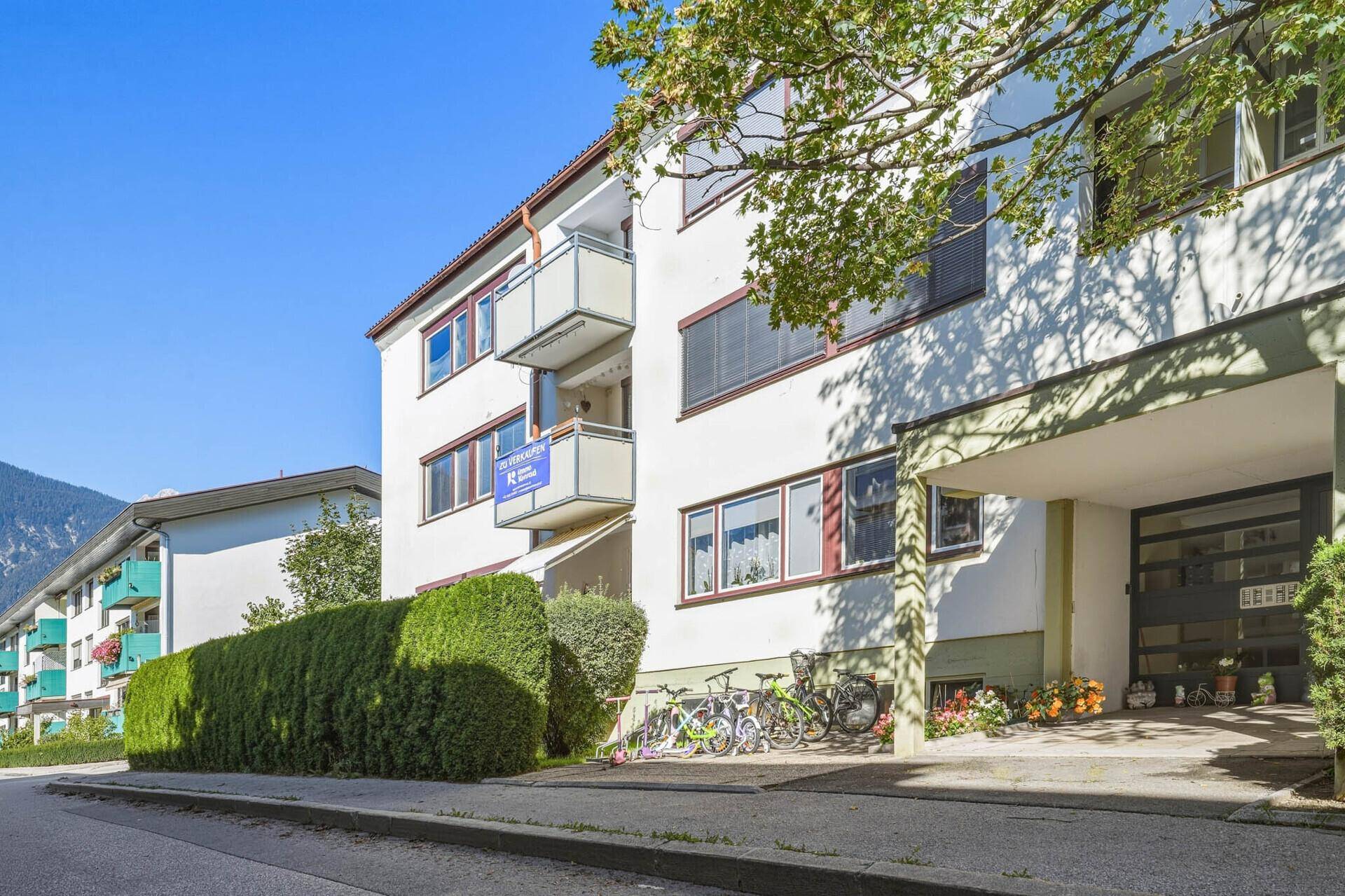 Mehrfamilienhaus mit Balkonen, grünen Hecken und gepflegter Außenanlage.
