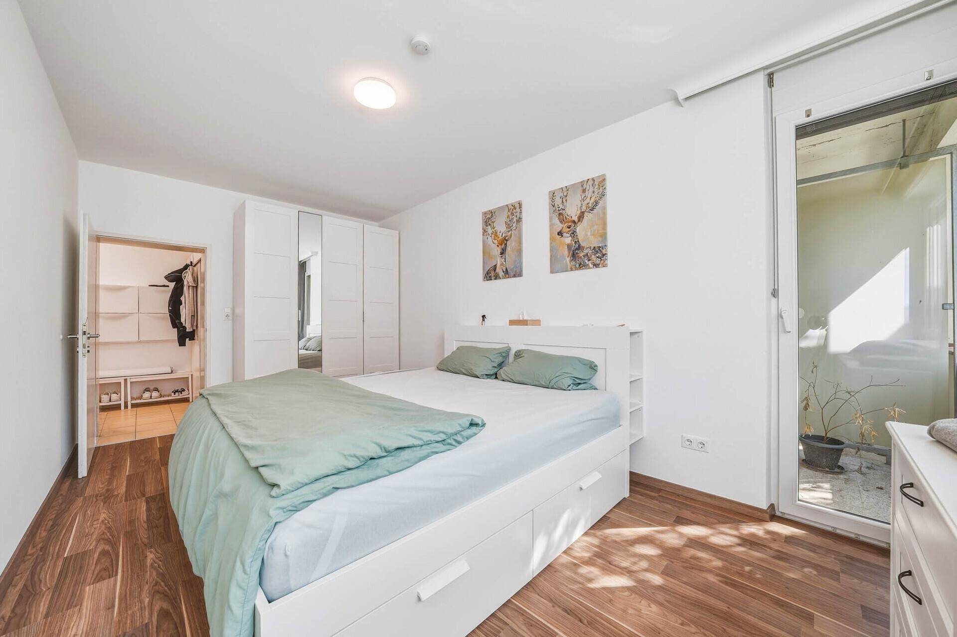 Schlafzimmer mit Holzboden, weißem Bett und Zugang zu einem kleinen Außenbereich.