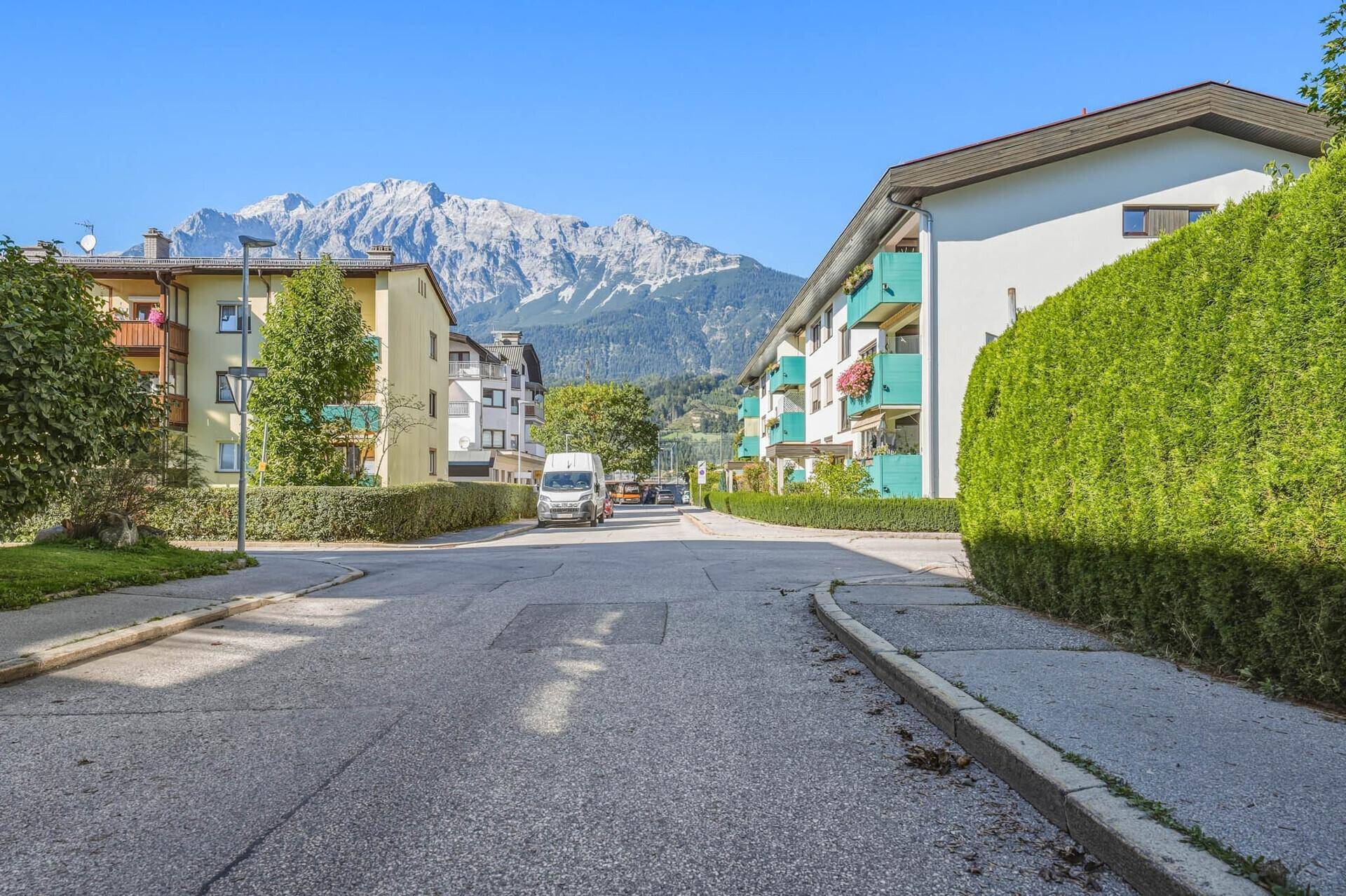 Wohnstraße mit gepflegten Hecken und Mehrfamilienhäusern vor einer beeindruckenden Bergkulisse.