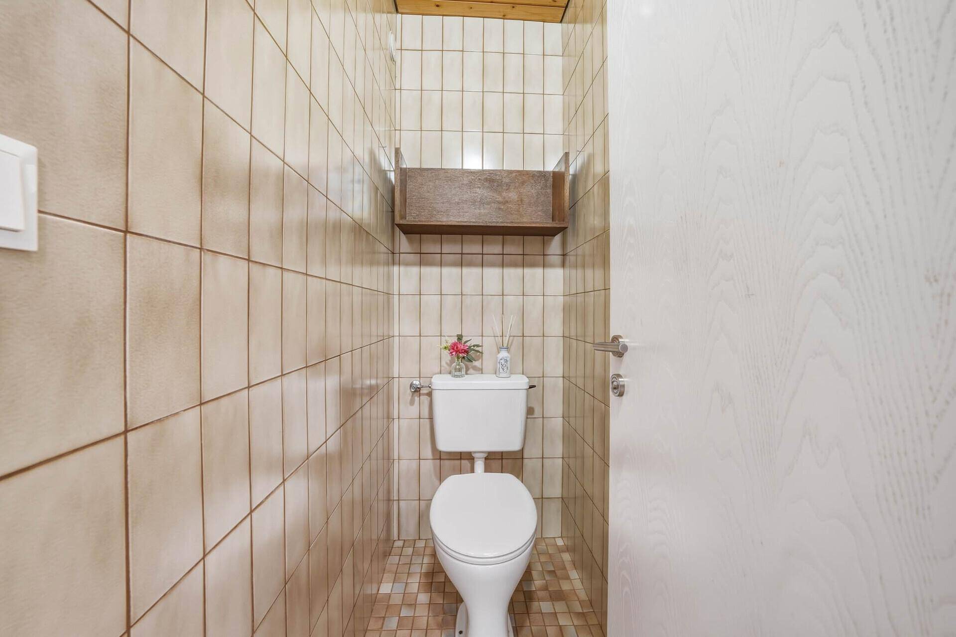 Separates WC mit Fliesen an den Wänden und einem einfachen Wandregal.