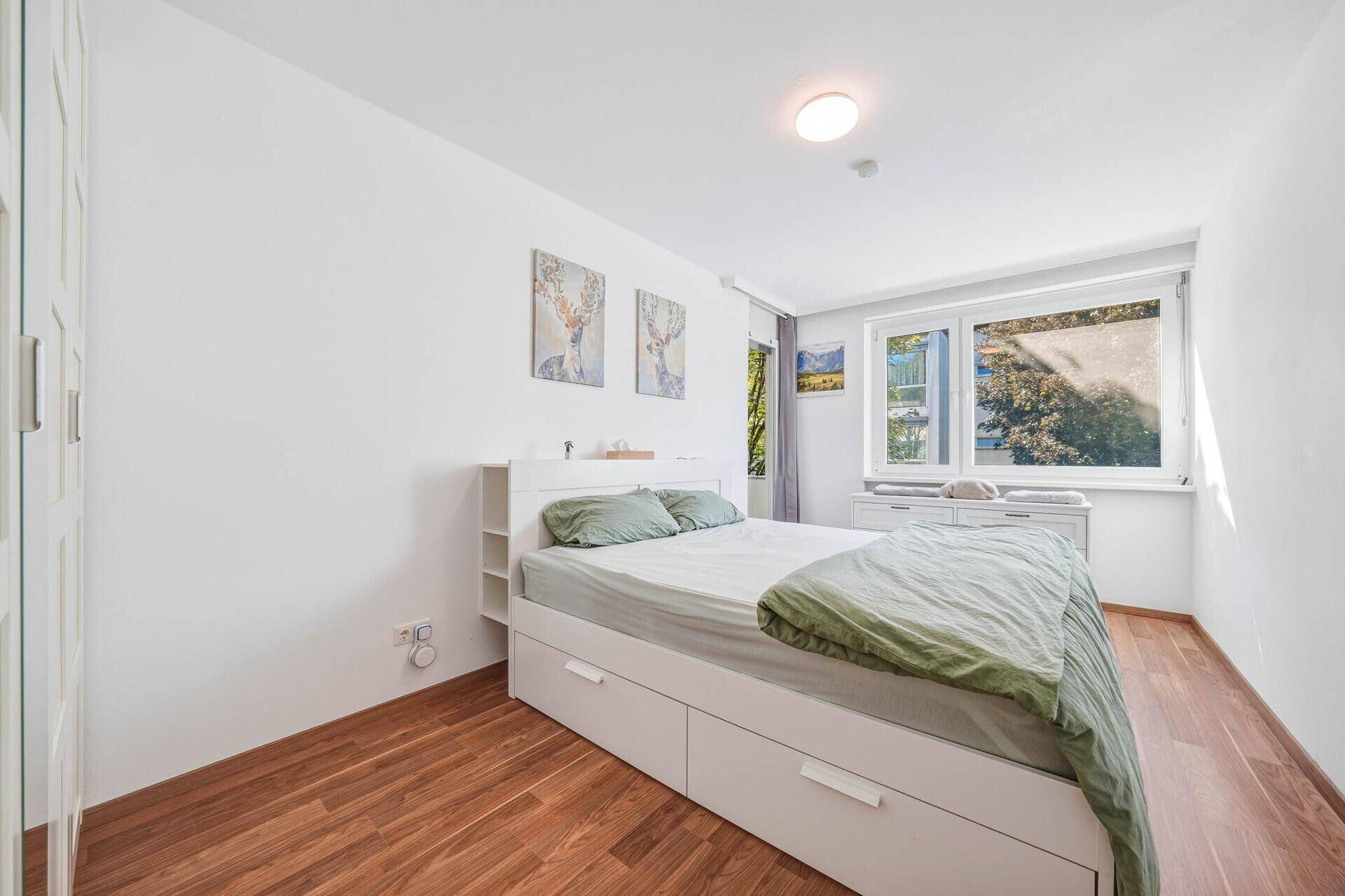 Helles Schlafzimmer mit weißem Bett, Holzboden und großem Fenster für viel Tageslicht.