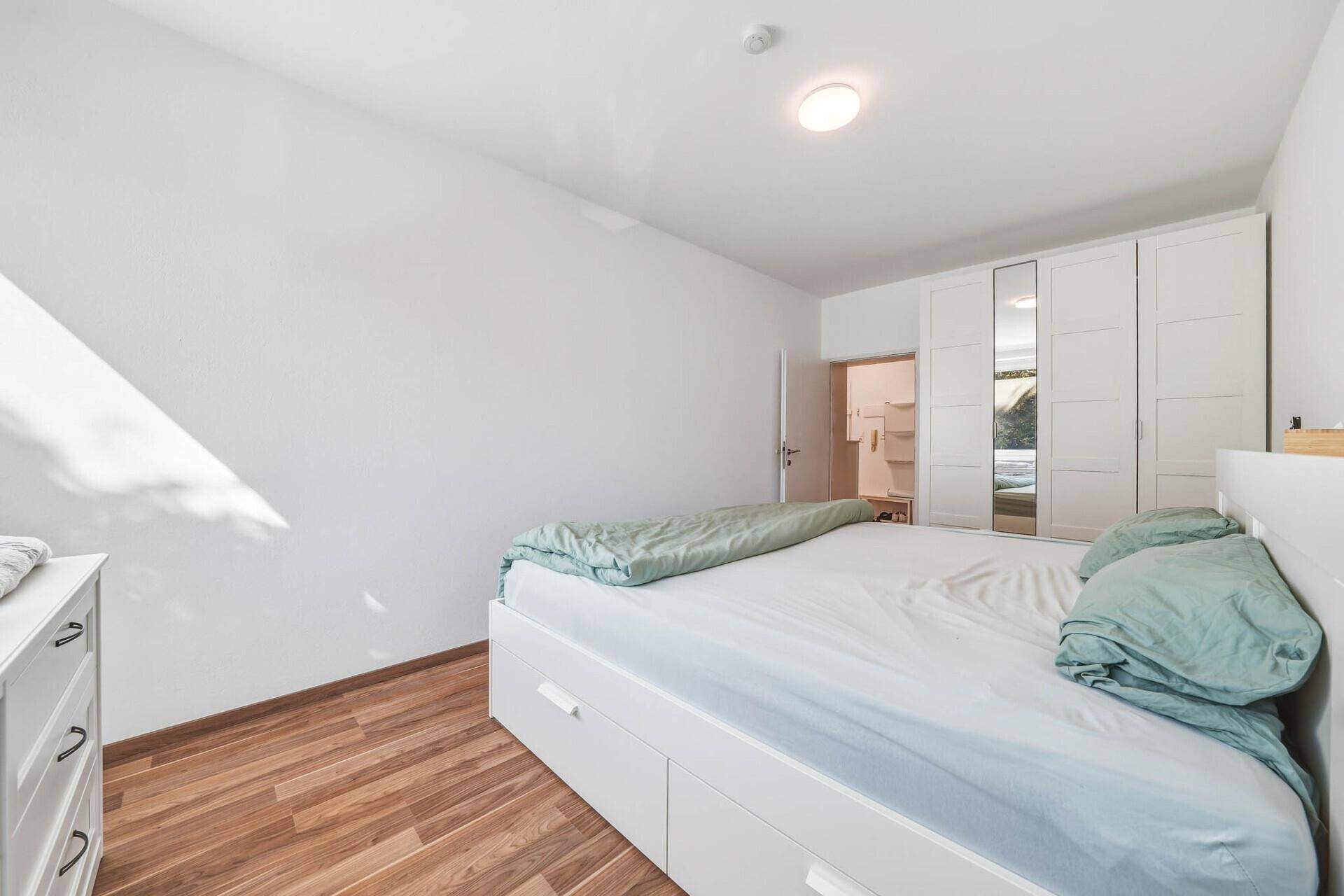 Geräumiges Schlafzimmer mit Holzboden, weißem Bett und großem Kleiderschrank mit Spiegeltüren.