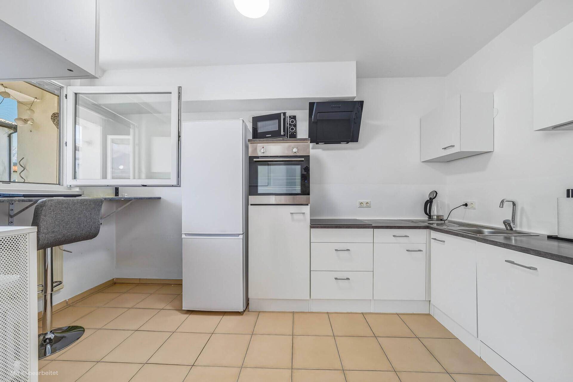 Moderne Küche mit weißen Schränken, dunklen Arbeitsplatten und einem Frühstücksbereich am Fenster.