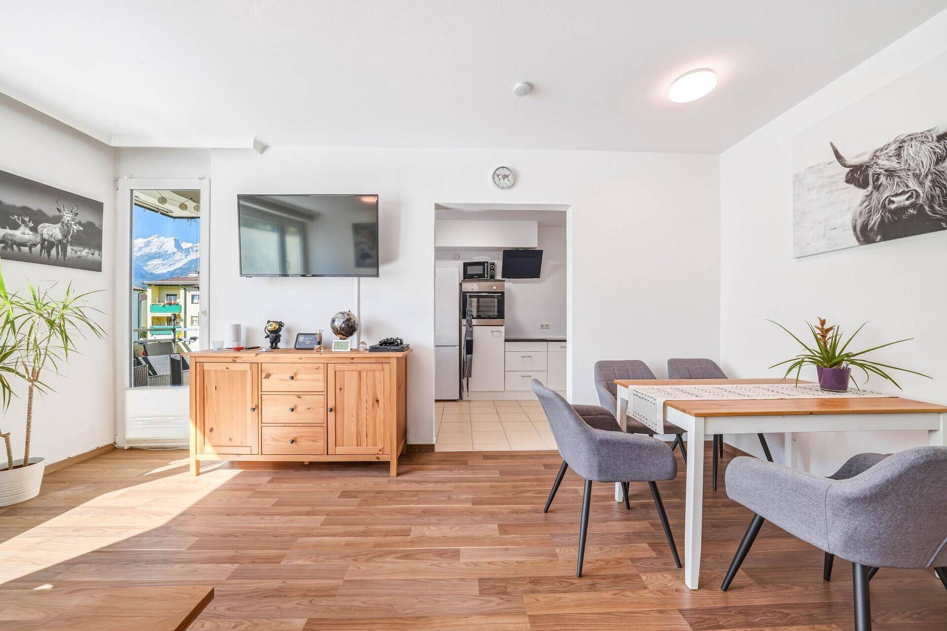 Wohn- und Essbereich mit Holzboden, Esstisch und Zugang zum Balkon mit Bergblick.