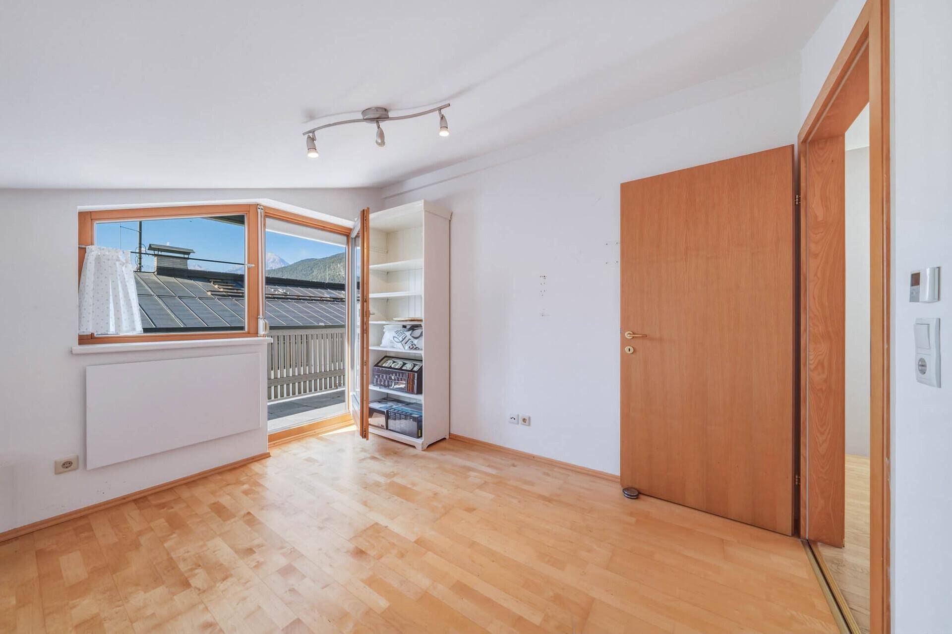 Schlafzimmer mit hellem Parkettboden, Fenster und Zugang zu einem Außenbereich.