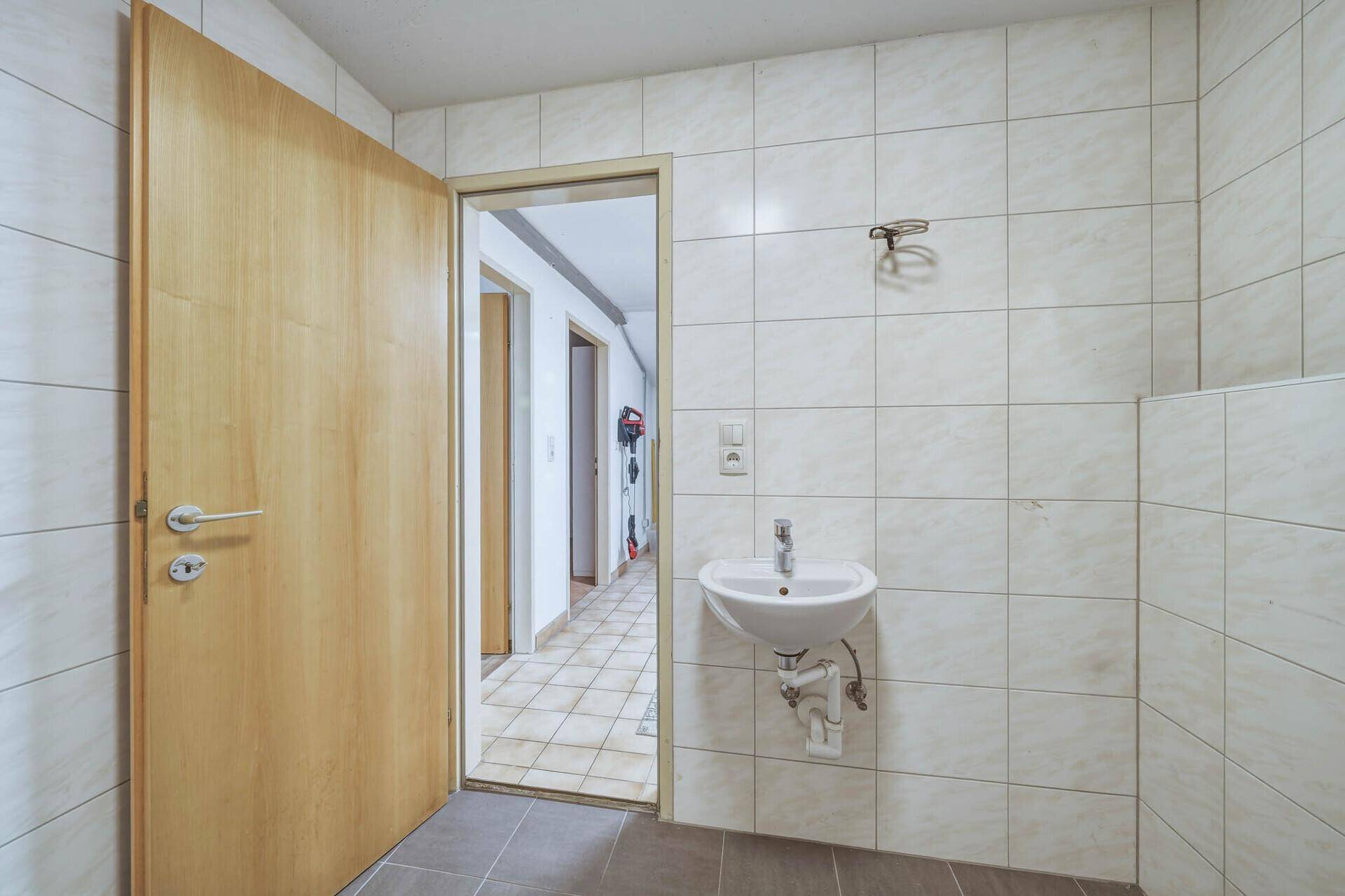 Kleines Gäste-WC mit weißen Fliesen, Waschbecken und Zugang zum Flur.