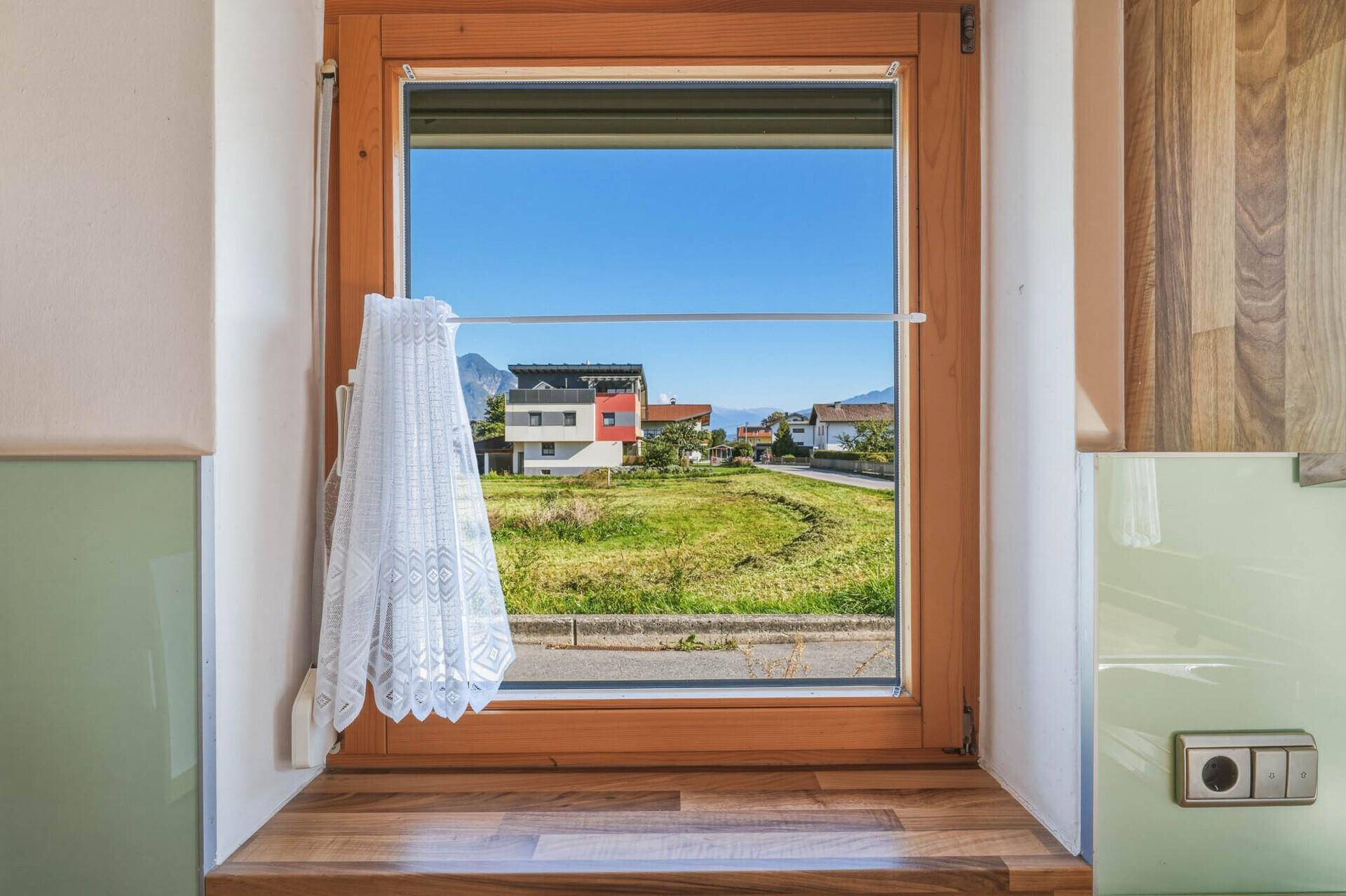 Blick aus dem Küchenfenster auf eine grüne Wiese und die umliegende Berglandschaft.