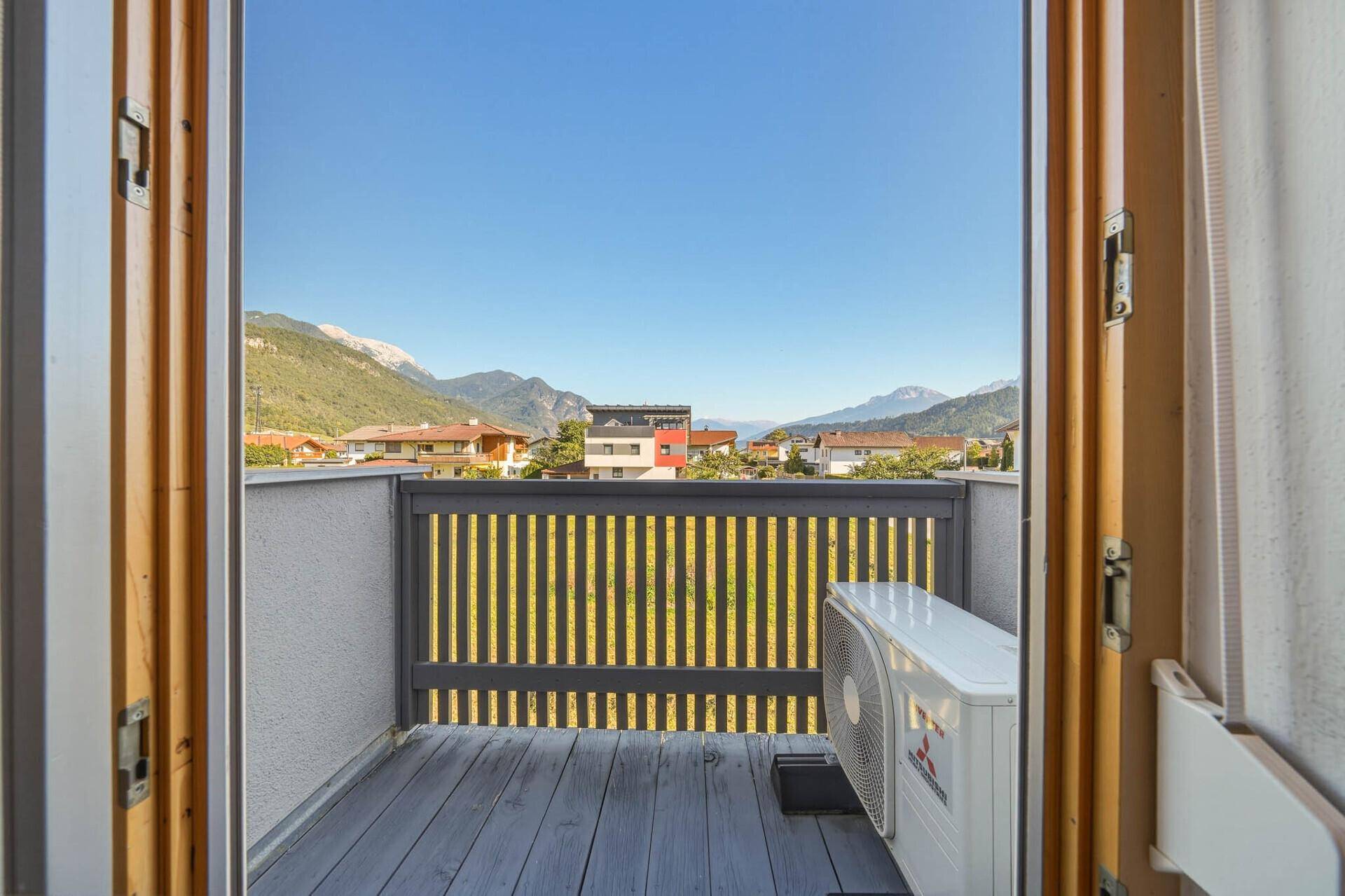 Balkon mit Holzboden, Geländer und Blick auf die Berge und umliegende Häuser.