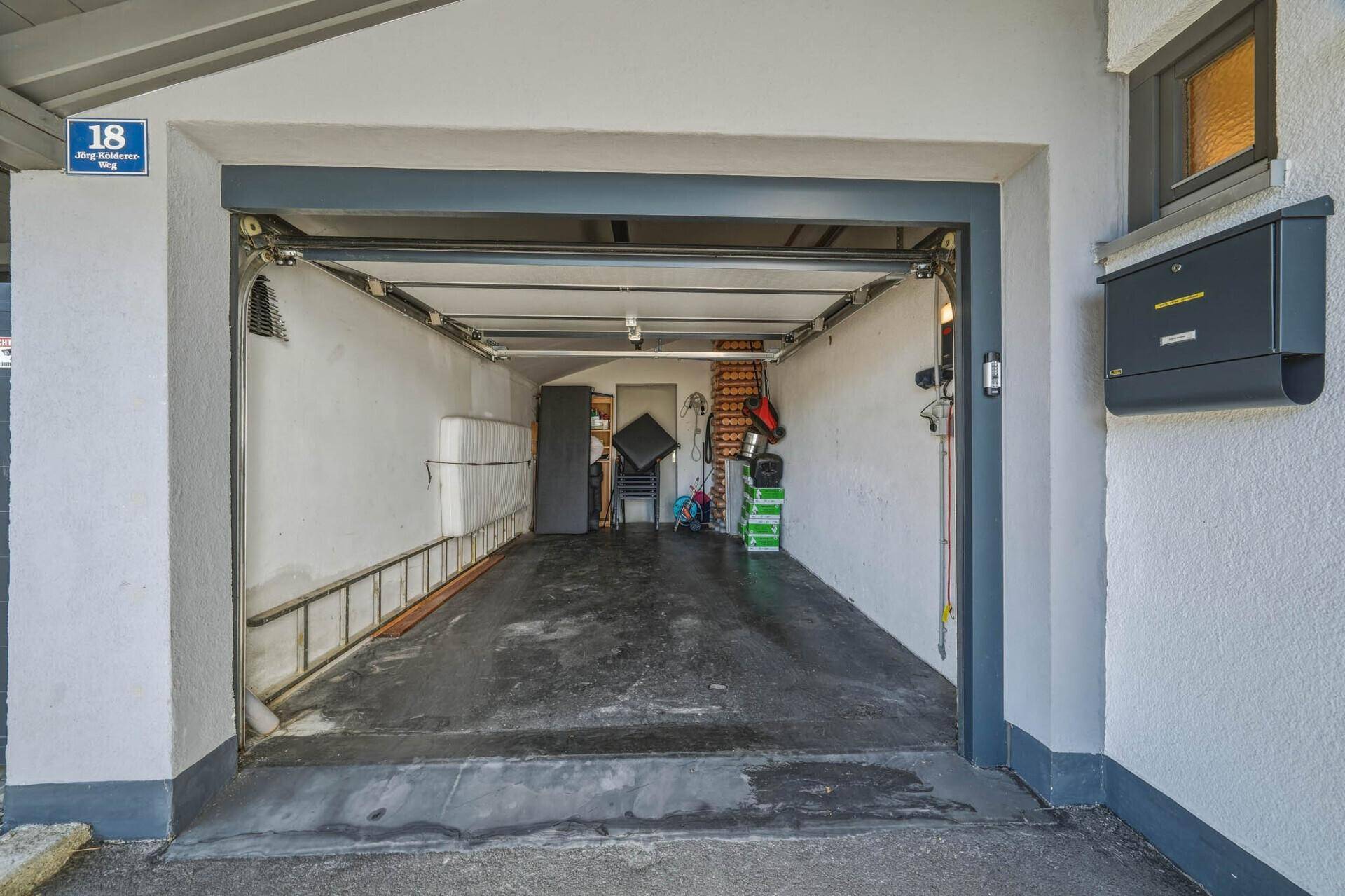 Offene Garage mit abschüssigem Boden und Stauraum für Fahrzeuge und Geräte.