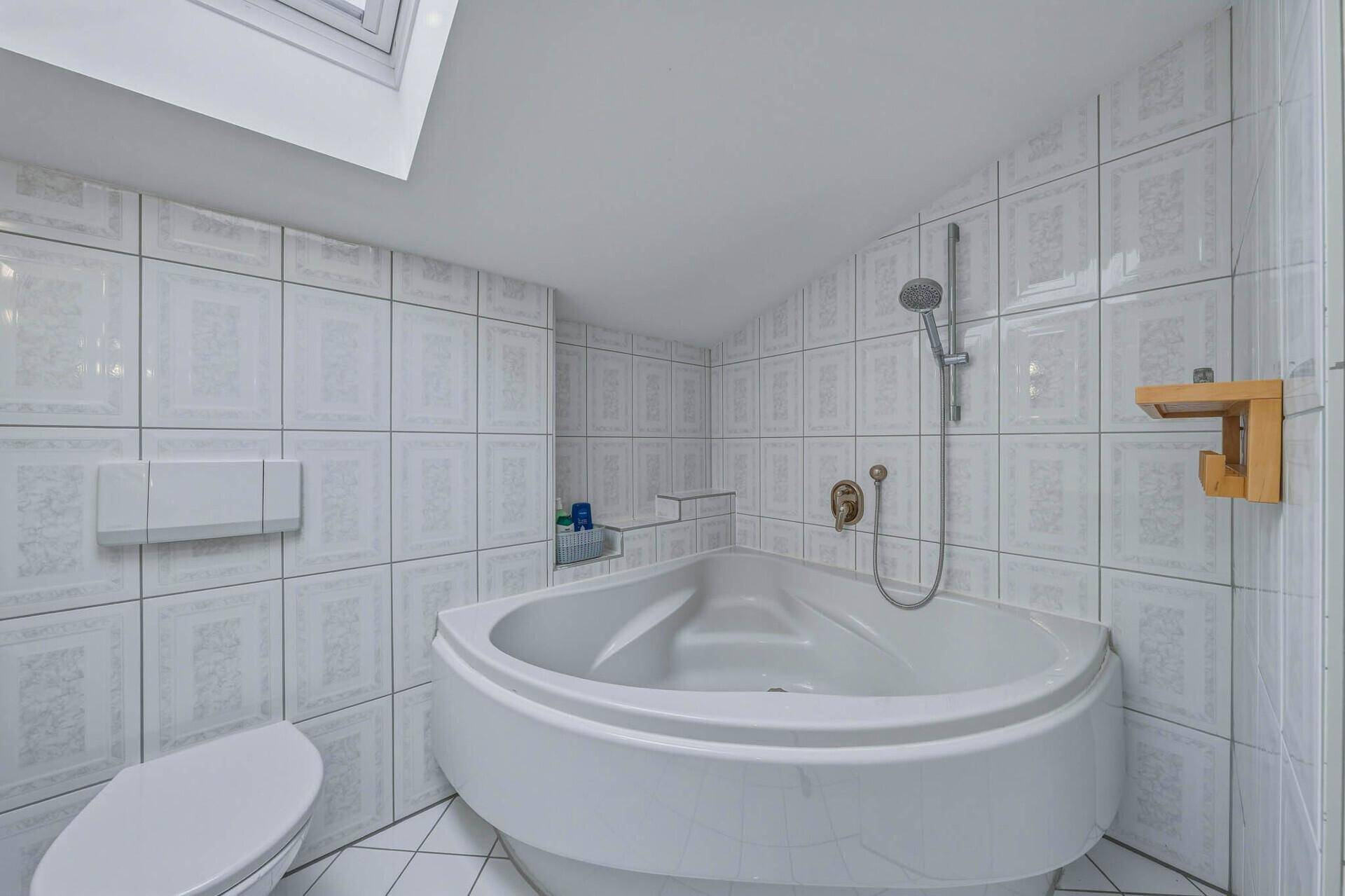 Badezimmer mit weißer Eckbadewanne, Duschfunktion und hellen Fliesen.