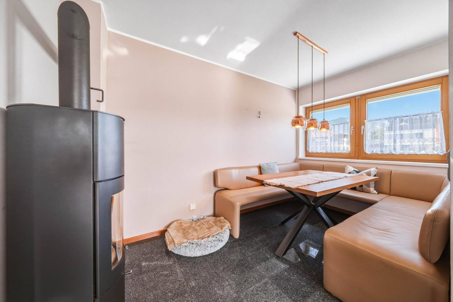 Gemütlicher Essbereich mit Eckbank, Esstisch und einem modernen Holzofen auf Fliesenboden.