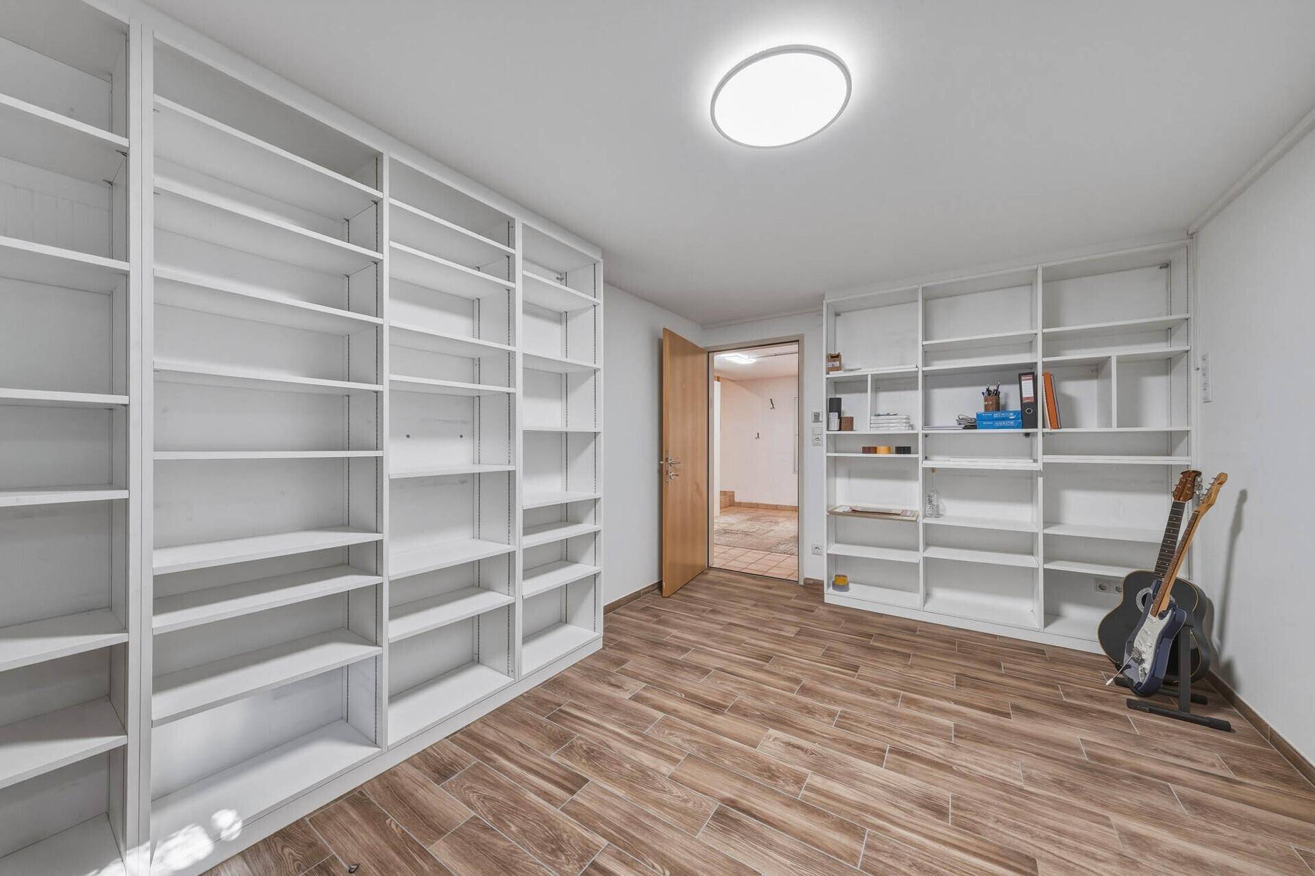 Heller Raum mit zahlreichen weißen Bücherregalen und Holzoptik-Laminatboden.