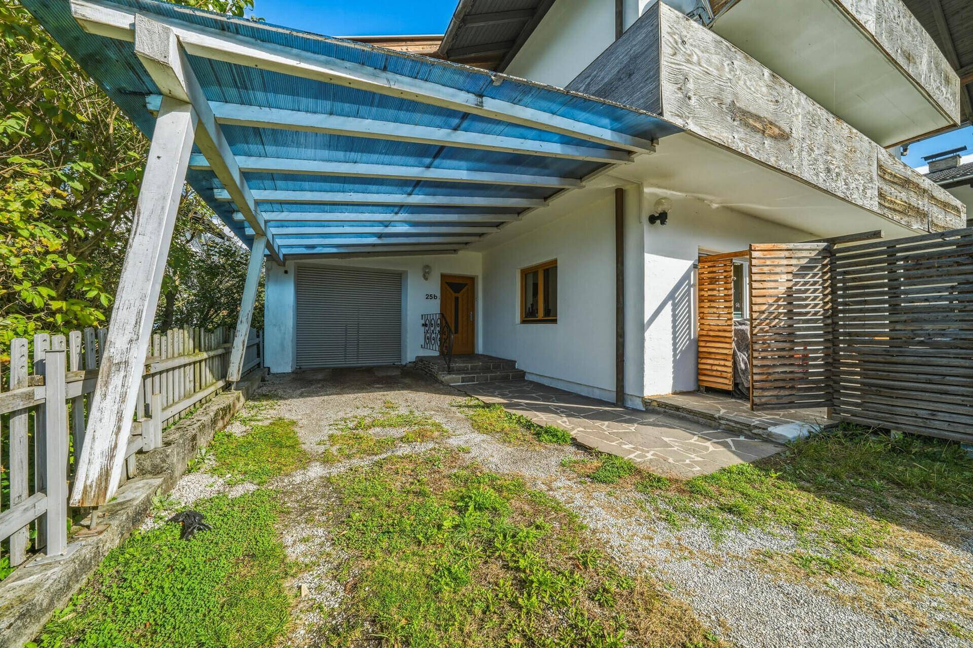 Eingangsbereich des Hauses mit überdachtem Carport und Zufahrt, umgeben von einem Holzzaun.