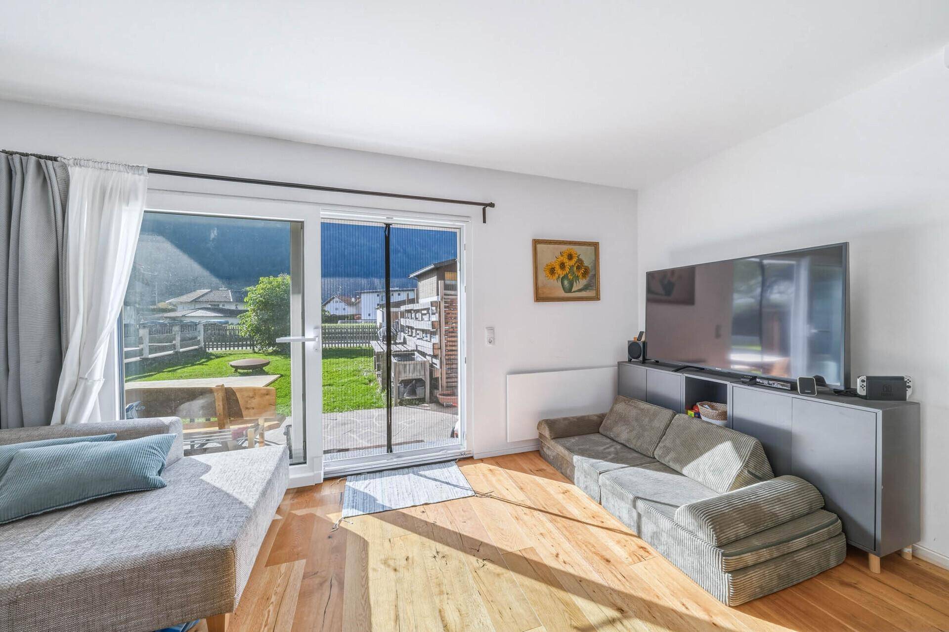 Gemütliches Wohnzimmer mit Sofa, Fernseher und Schiebetür zum Garten, mit Blick auf die Berge.
