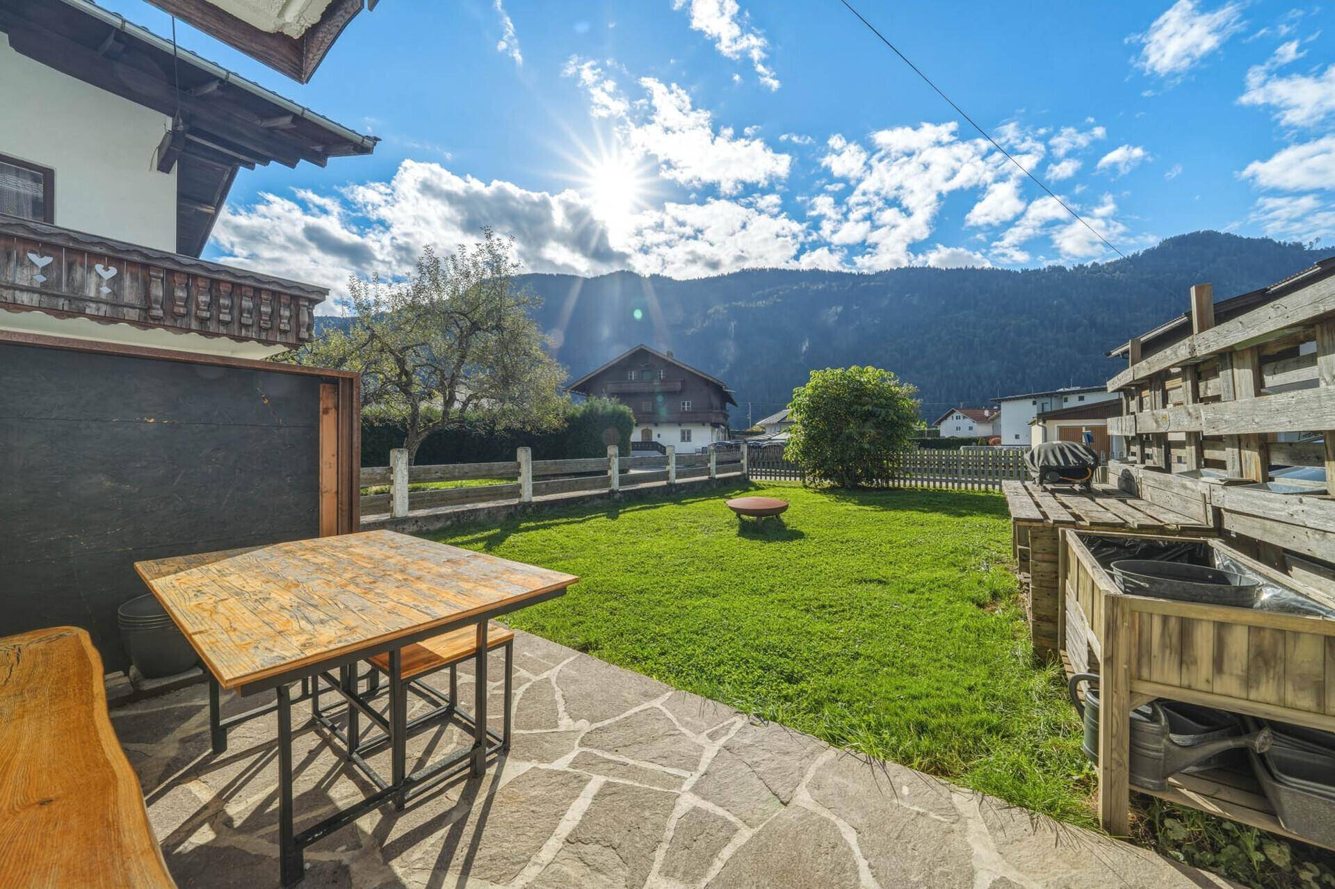 Sonniger Außenbereich mit Steinterrasse, Rasenfläche und Bergblick, ideal für Entspannung im Freien.