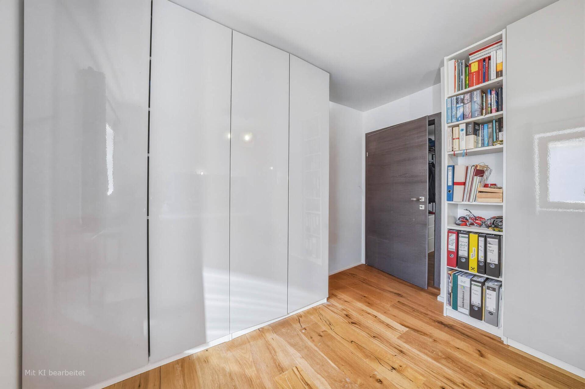 Schlafzimmer mit modernen weißen Schränken und einem Bücherregal, das zusätzlichen Stauraum bietet.