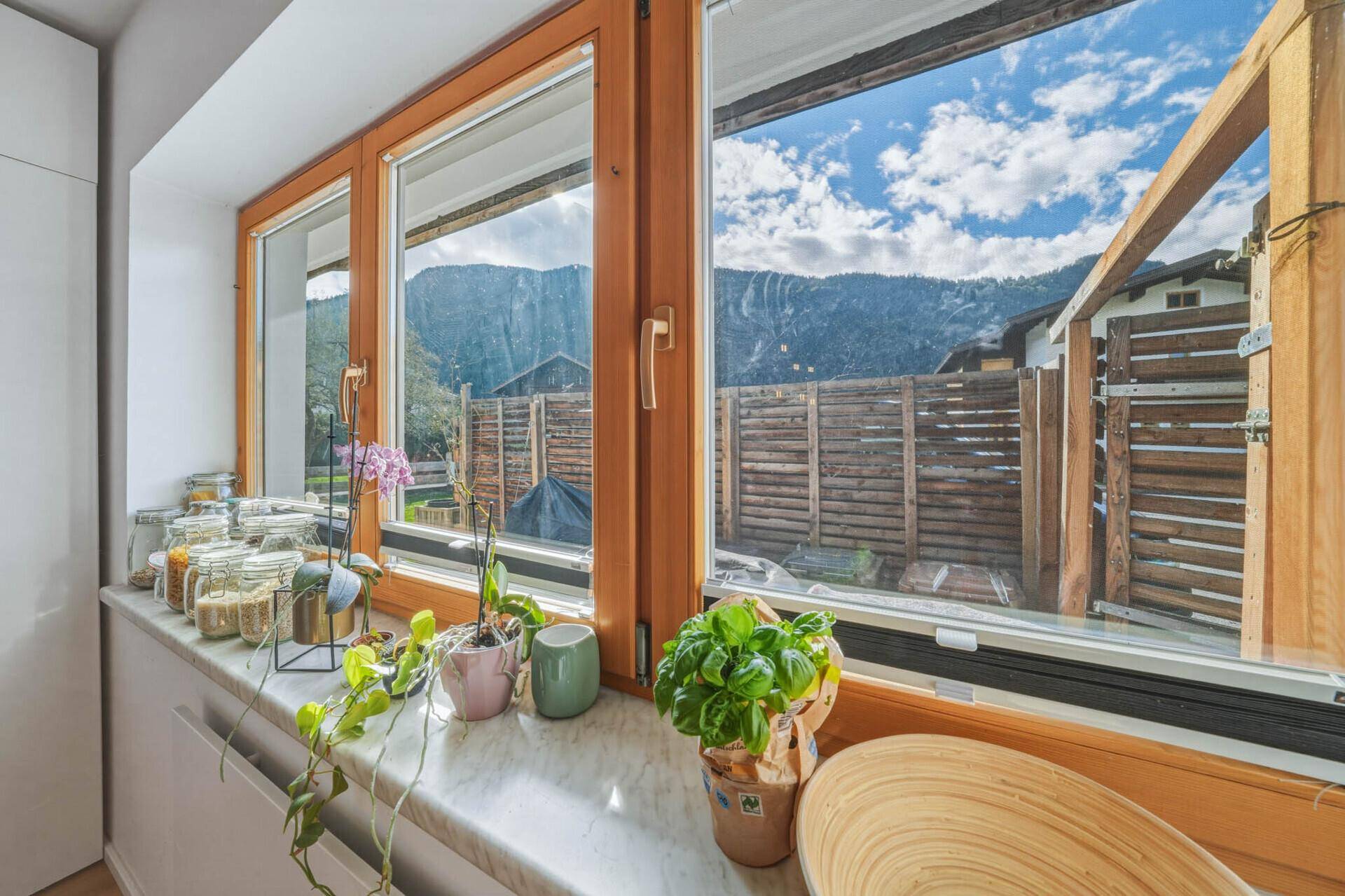Fenster in der Küche mit Pflanzen auf der Fensterbank und einem weiten Blick auf die Berge.