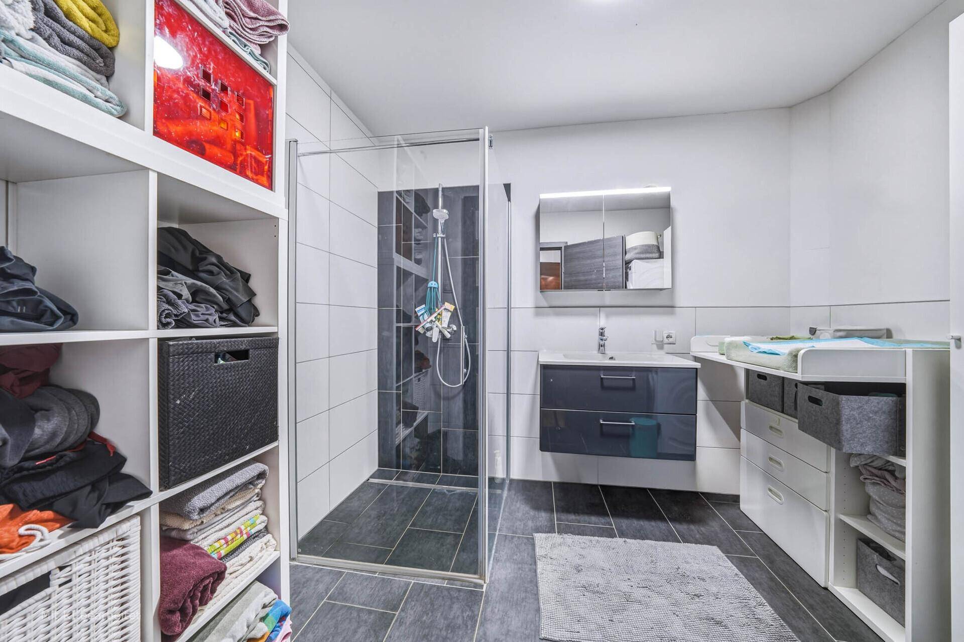 Modernes Badezimmer mit ebenerdiger Dusche, Waschtisch und praktischen Ablageregalen.