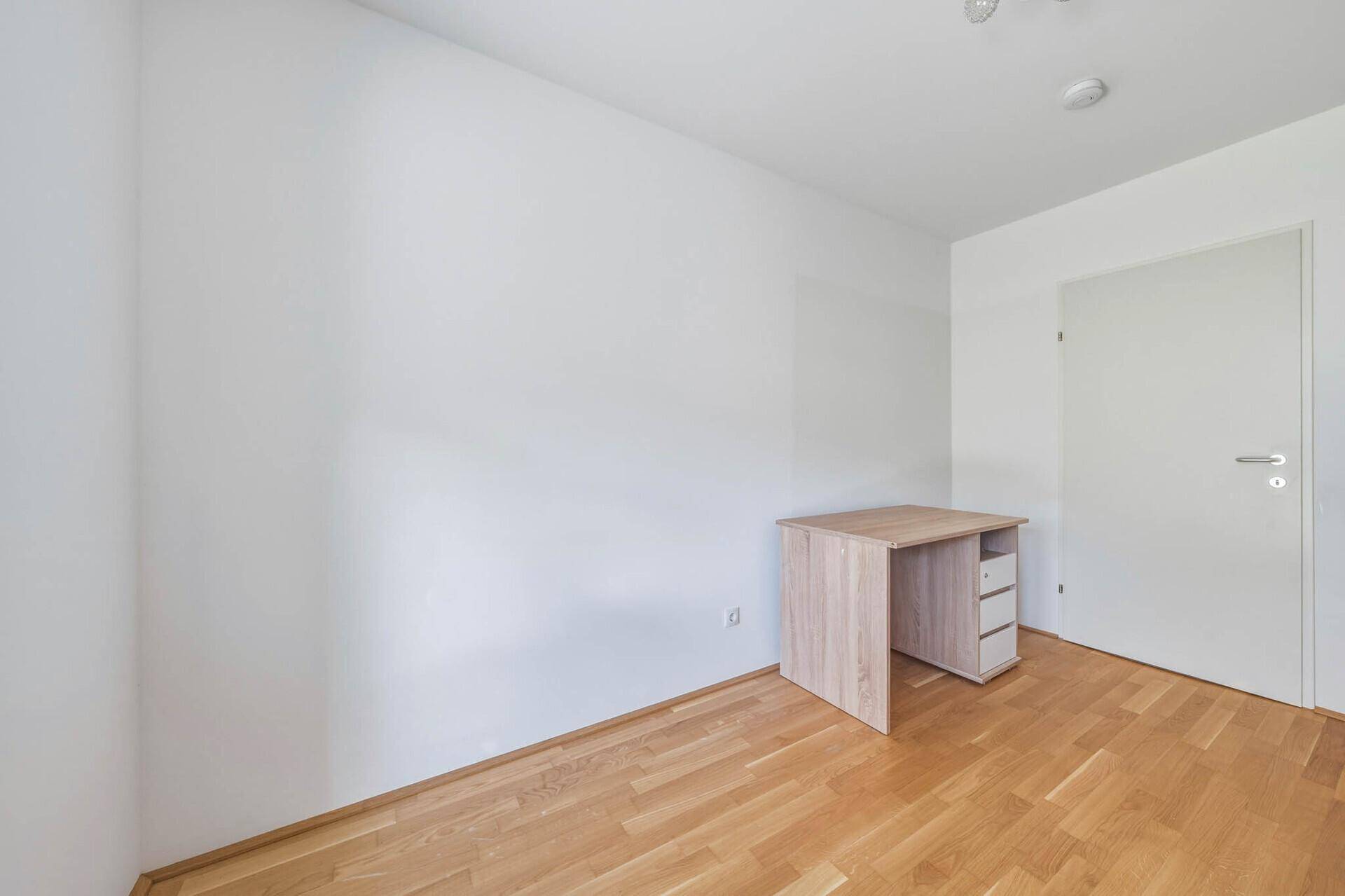 Helles Arbeitszimmer mit Parkettboden und einem einfachen Schreibtisch, ideal für Home-Office.
