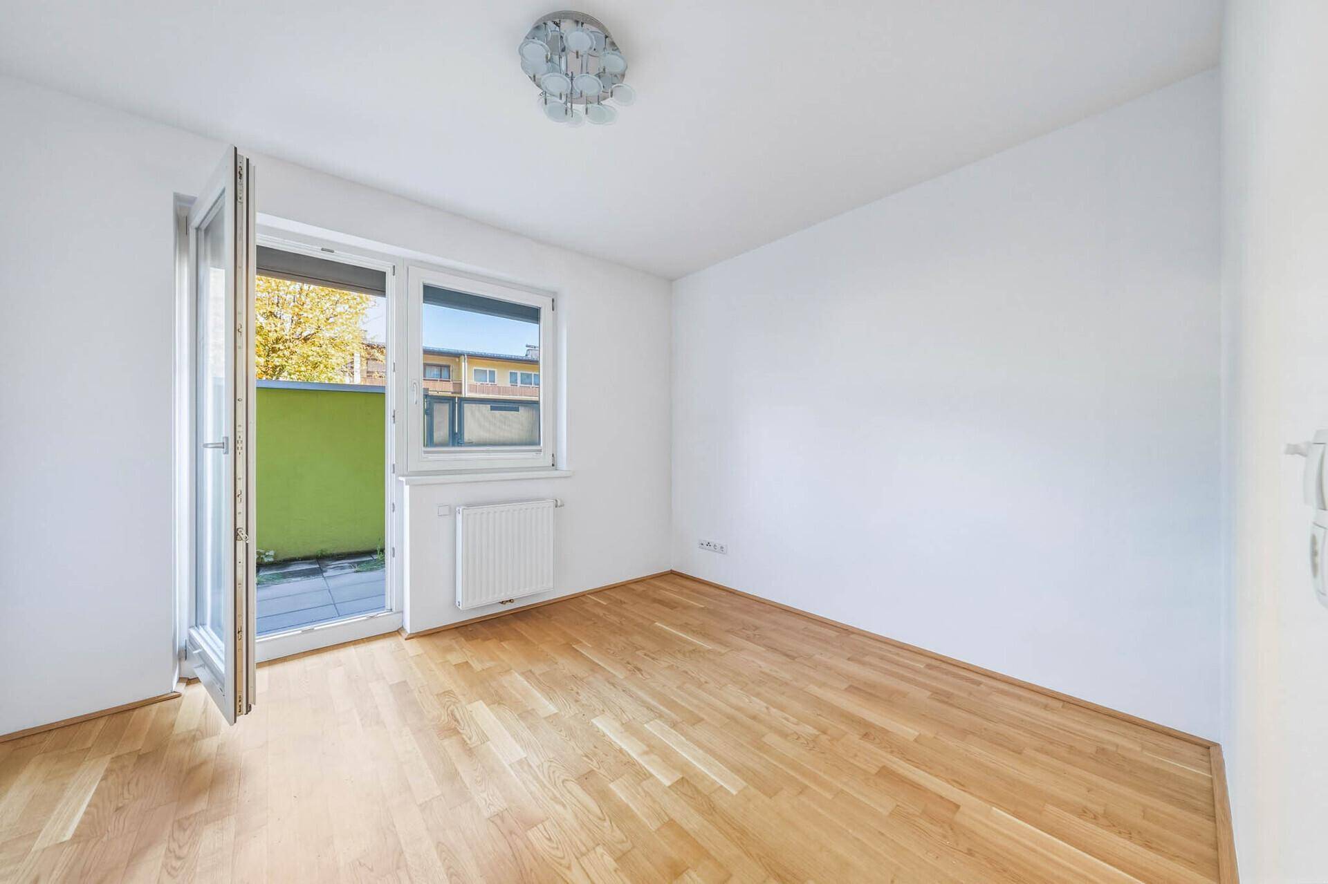 Helles Schlafzimmer mit Parkettboden und offenem Zugang zu einem Außenbereich.