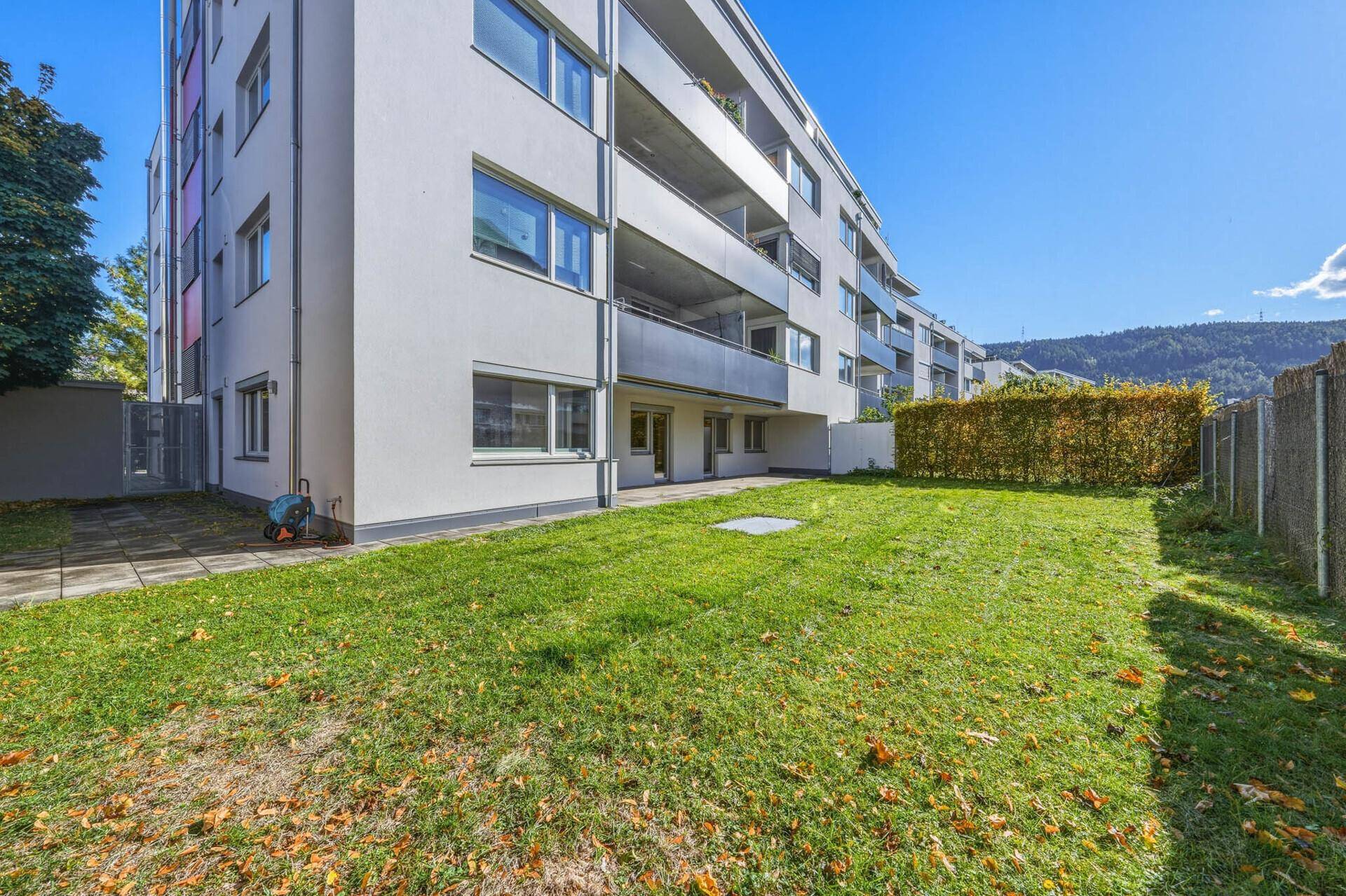 Große Rasenfläche vor dem modernen Wohngebäude mit Balkonen und einer Hecke.