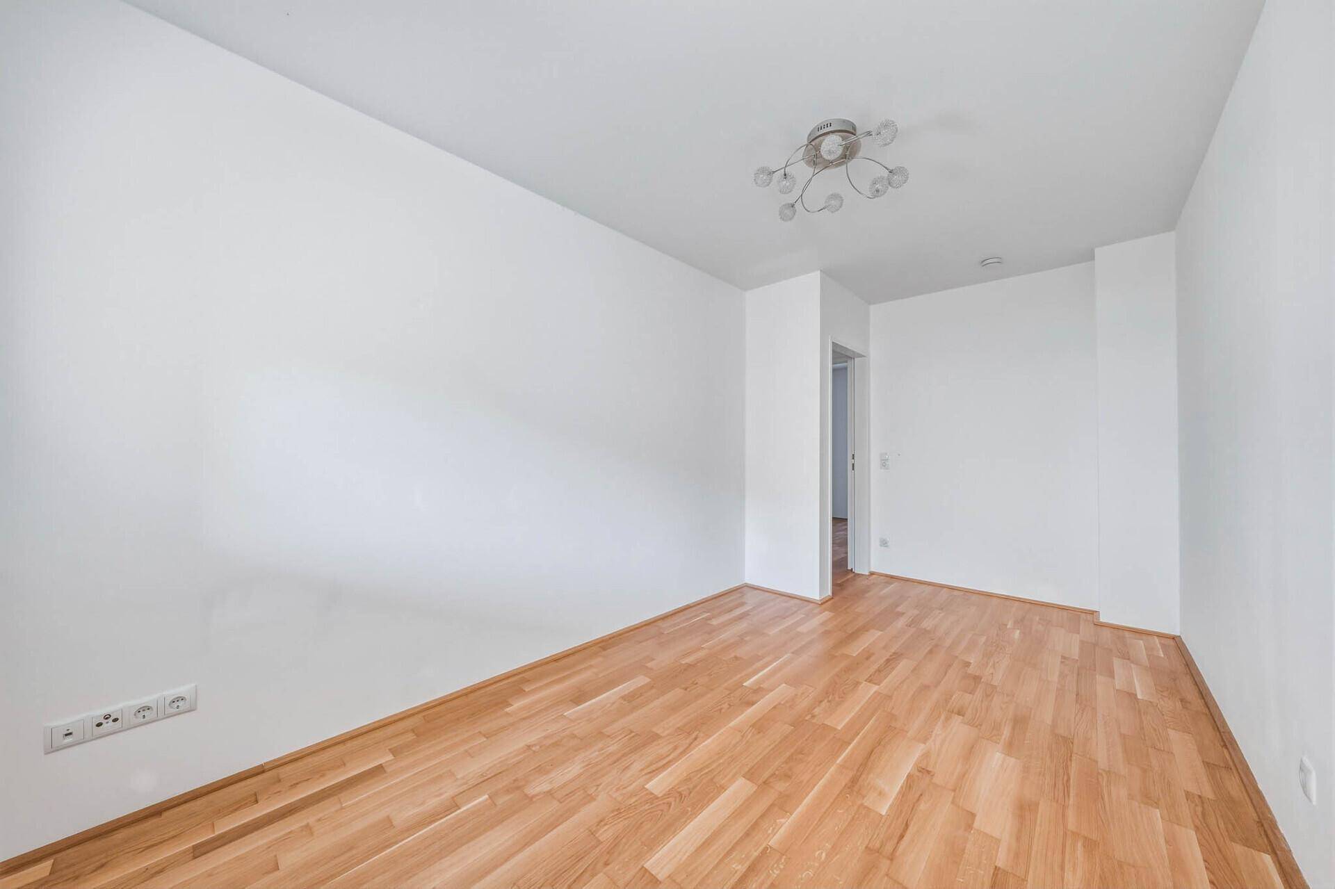 Helles Schlafzimmer mit Parkettboden und weiß gestrichenen Wänden, bereit zur Einrichtung.