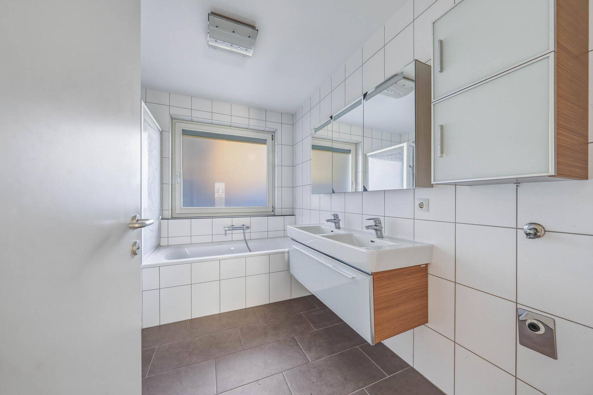 Modernes Badezimmer mit Doppelwaschbecken, Badewanne und Fenster für Tageslicht.