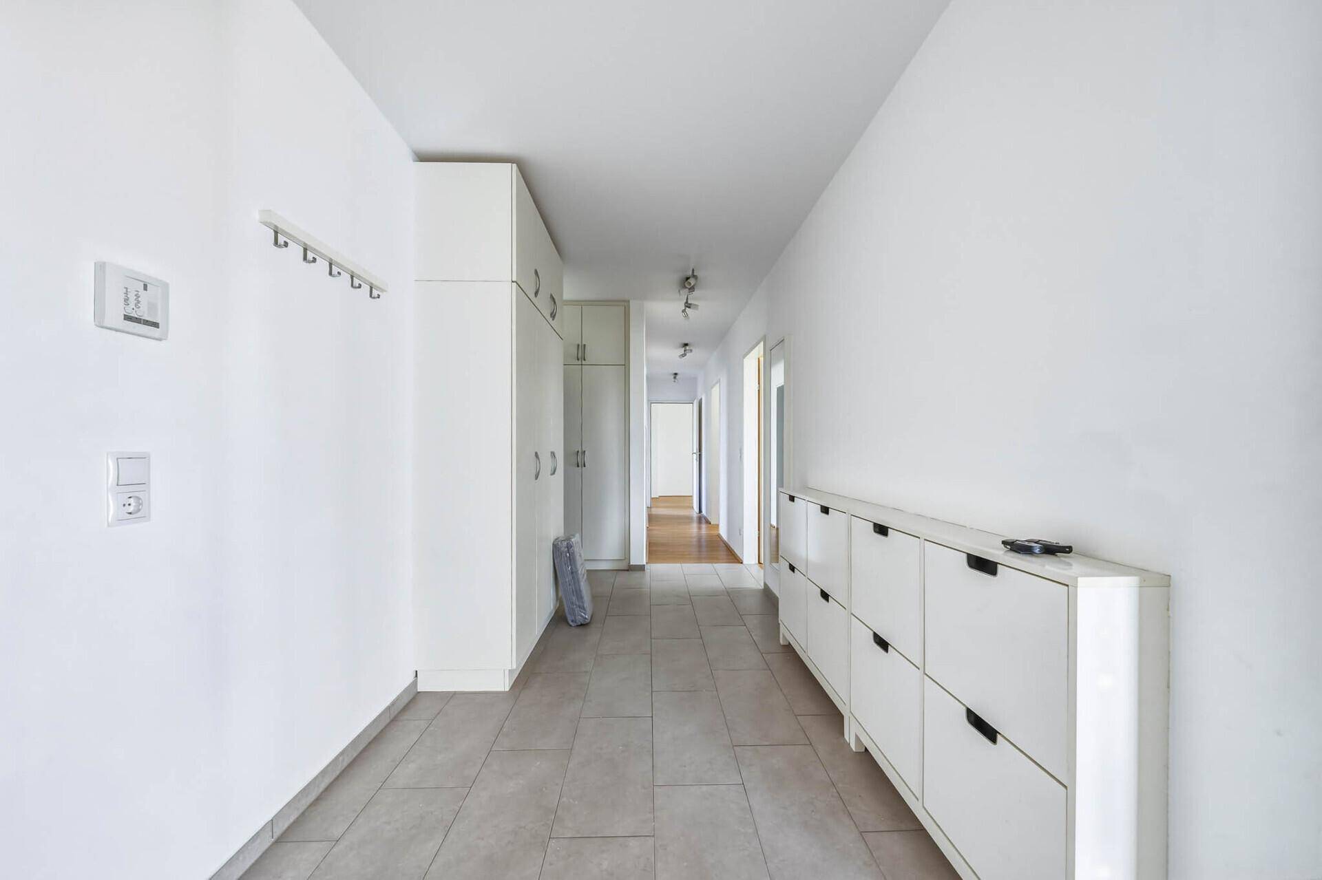 Langer Flur mit Fliesenboden, Einbauschränken und Garderobe.