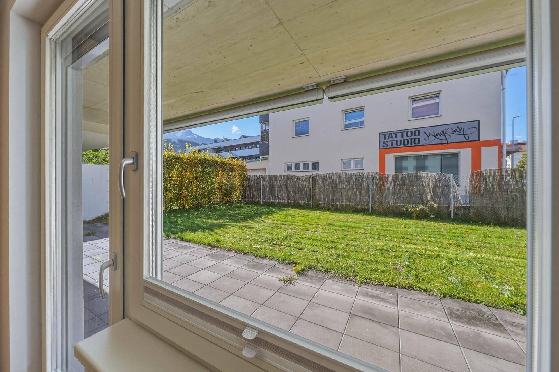 Blick aus dem Fenster auf den gepflegten Gartenbereich mit Rasen und Hecke.