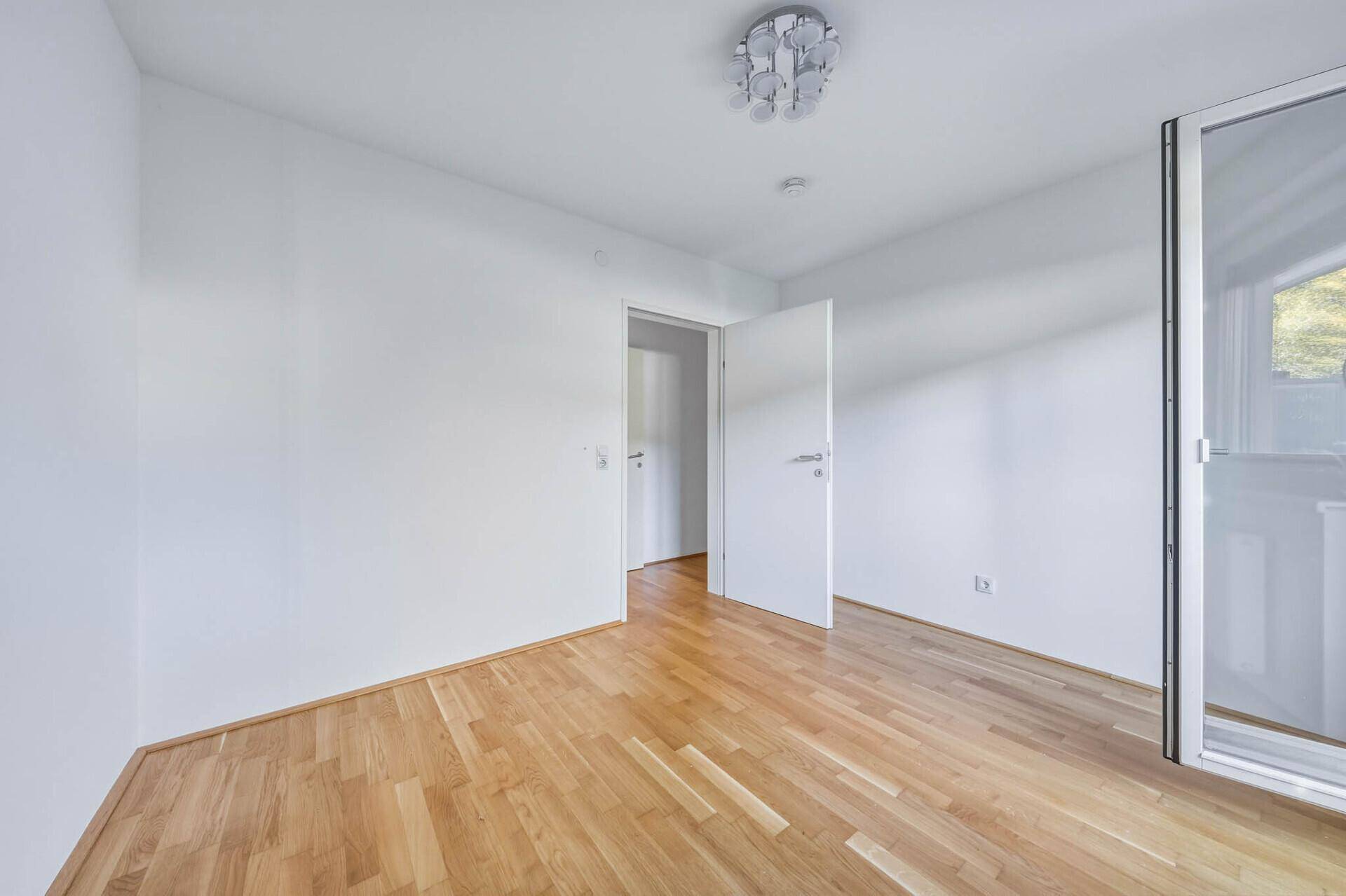 Leeres Schlafzimmer mit Parkettboden und weiß gestrichenen Wänden, bereit zur individuellen Gestaltung.