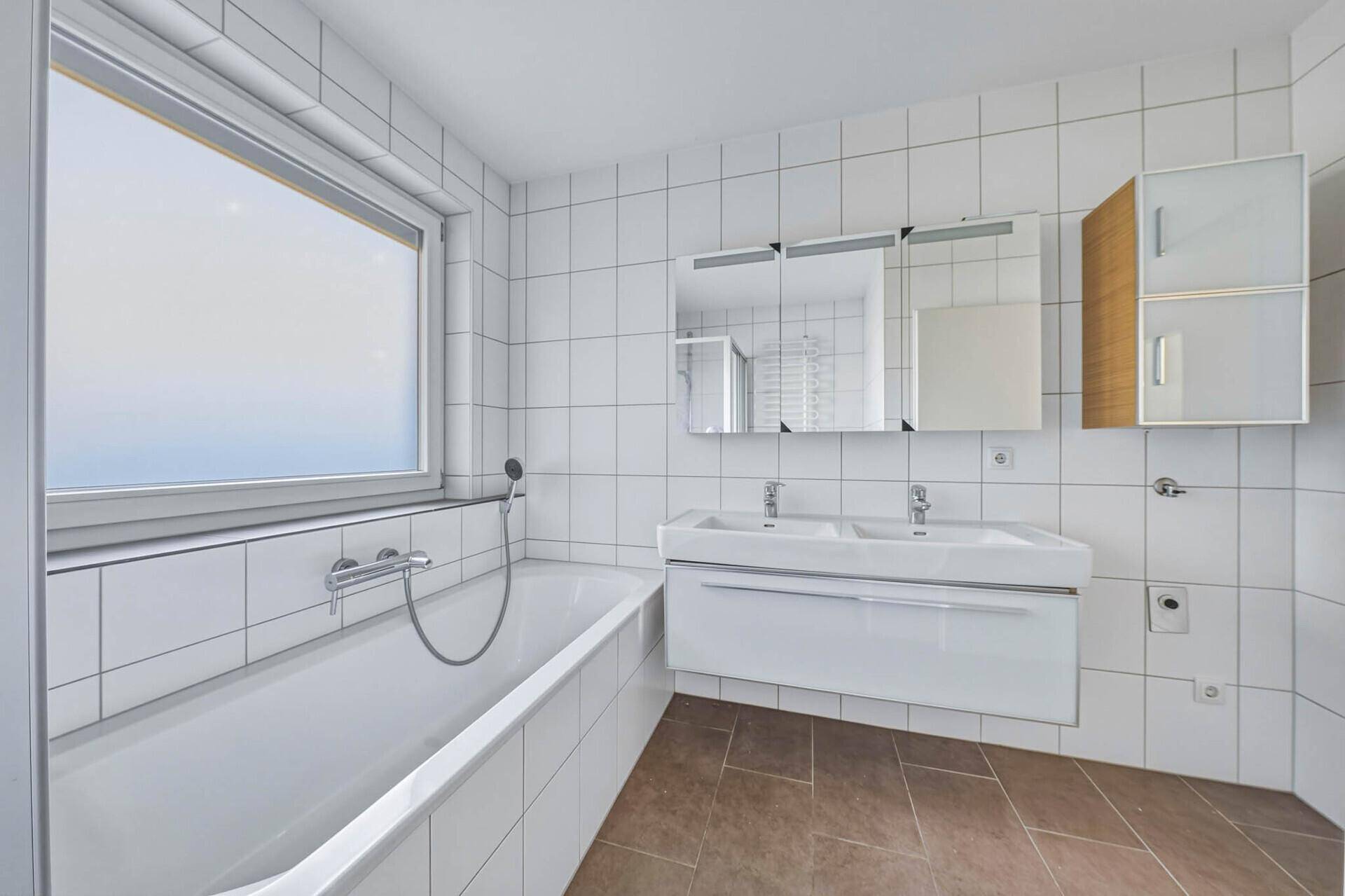 Helles Badezimmer mit Badewanne, Doppelwaschbecken und Spiegelschrank.