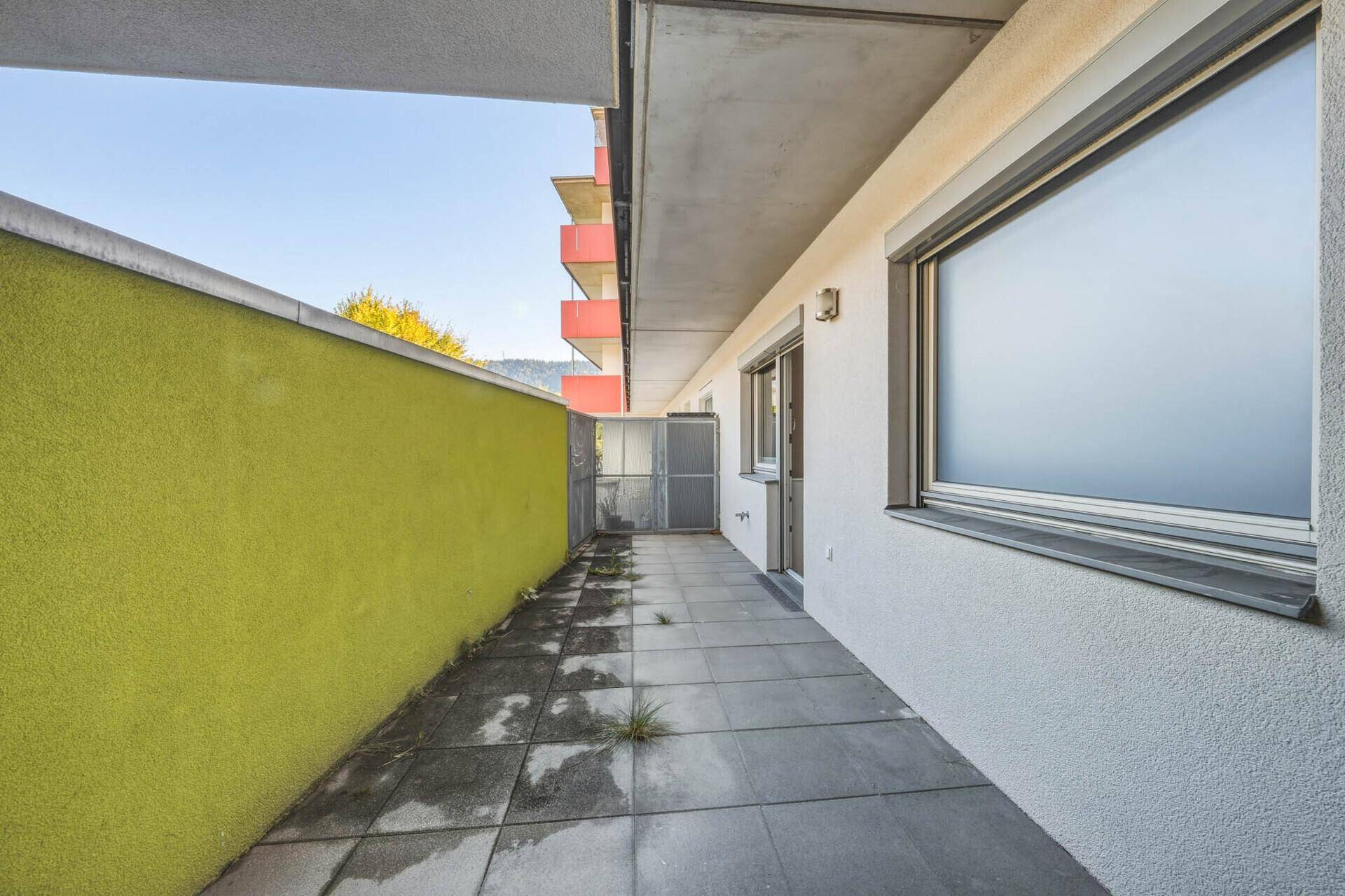 Lange, schmale Terrasse mit grüner Wand und Blick auf die Gebäudefassade.