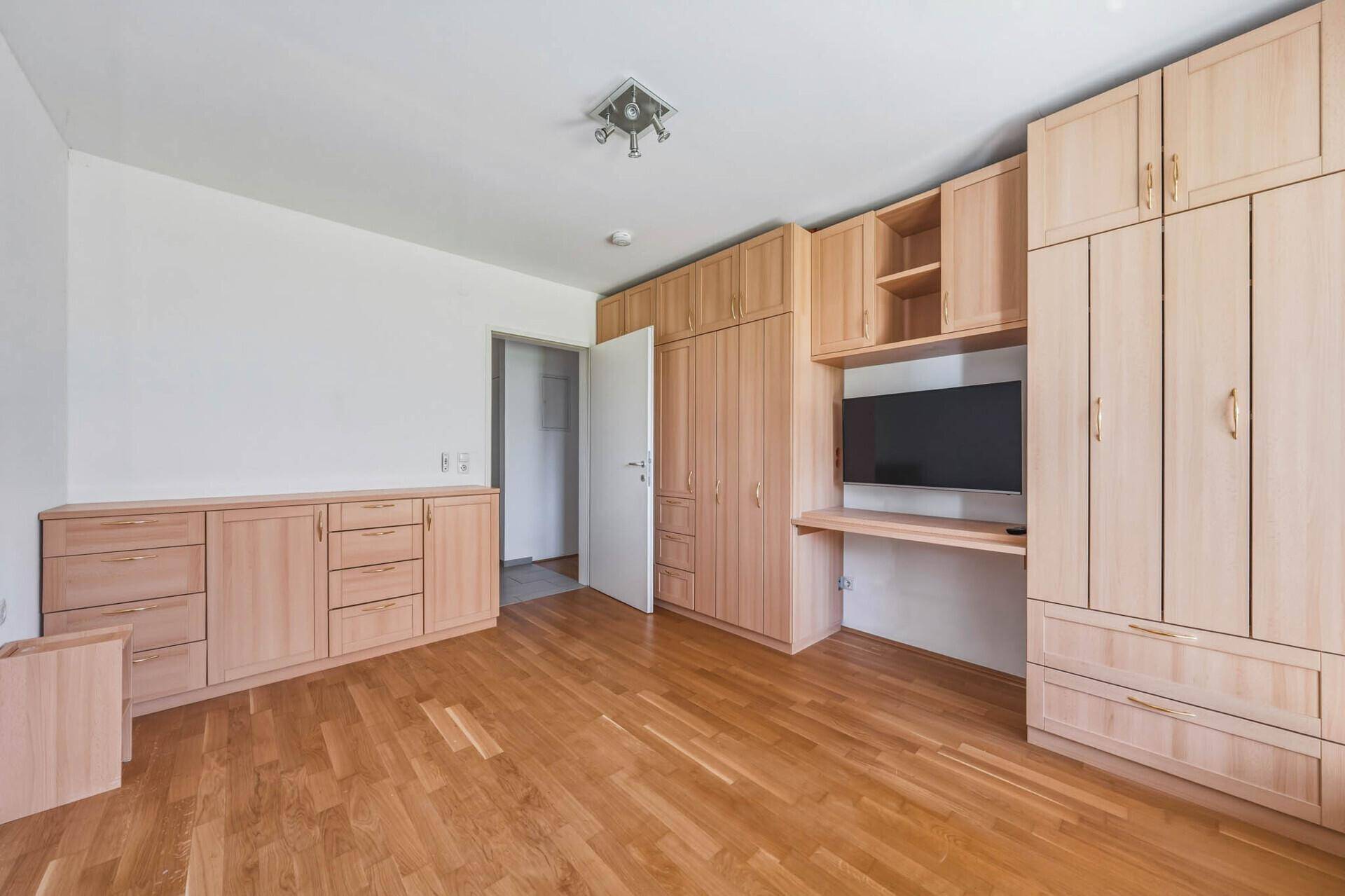 Schlafzimmer mit maßgefertigten Holzschränken, integriertem Schreibtisch und Parkettboden.